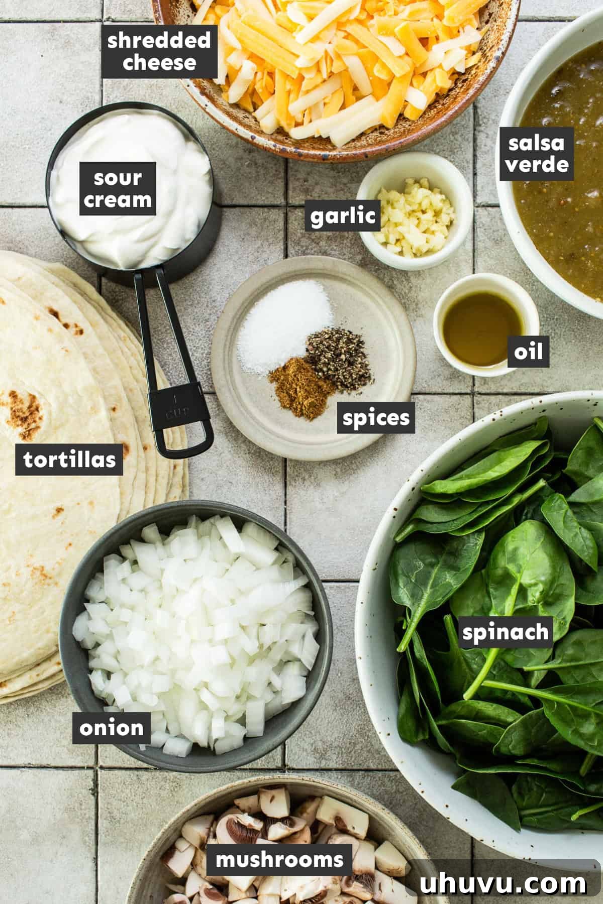 Creamy Spinach Enchiladas 3 Fresh ingredients for spinach and mushroom enchiladas, including spinach, mushrooms, onions, garlic, sour cream, cheese, and salsa verde, arranged on a rustic wooden table.
