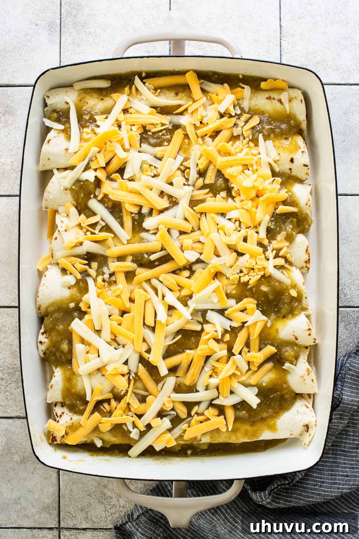 Creamy Spinach Enchiladas 6 A baking dish filled with assembled spinach enchiladas, generously topped with vibrant green salsa verde and a layer of shredded cheese, ready for baking.