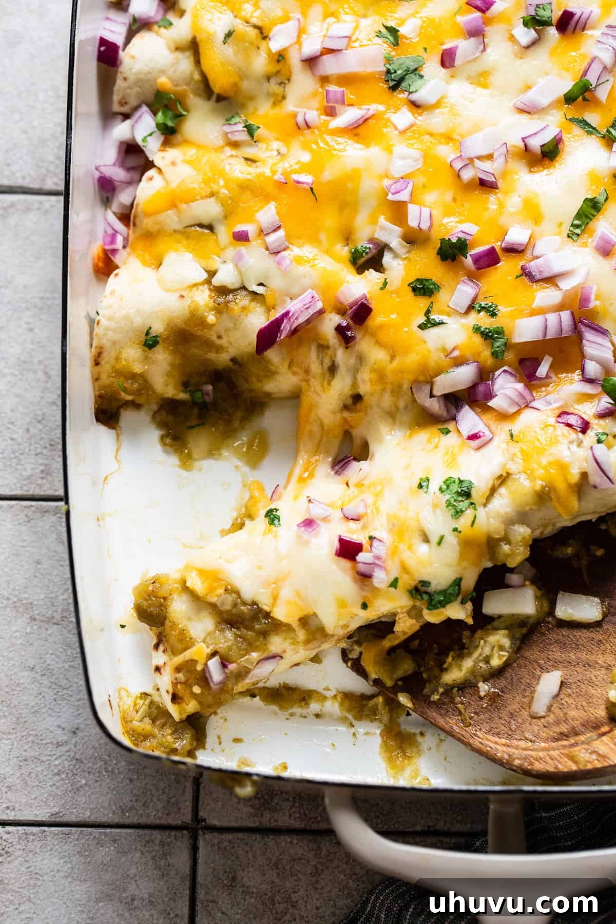 Creamy Spinach Enchiladas 8 A wooden spatula carefully lifting a cheesy, sauce-covered spinach enchilada from a baking dish, highlighting its delicious layers.