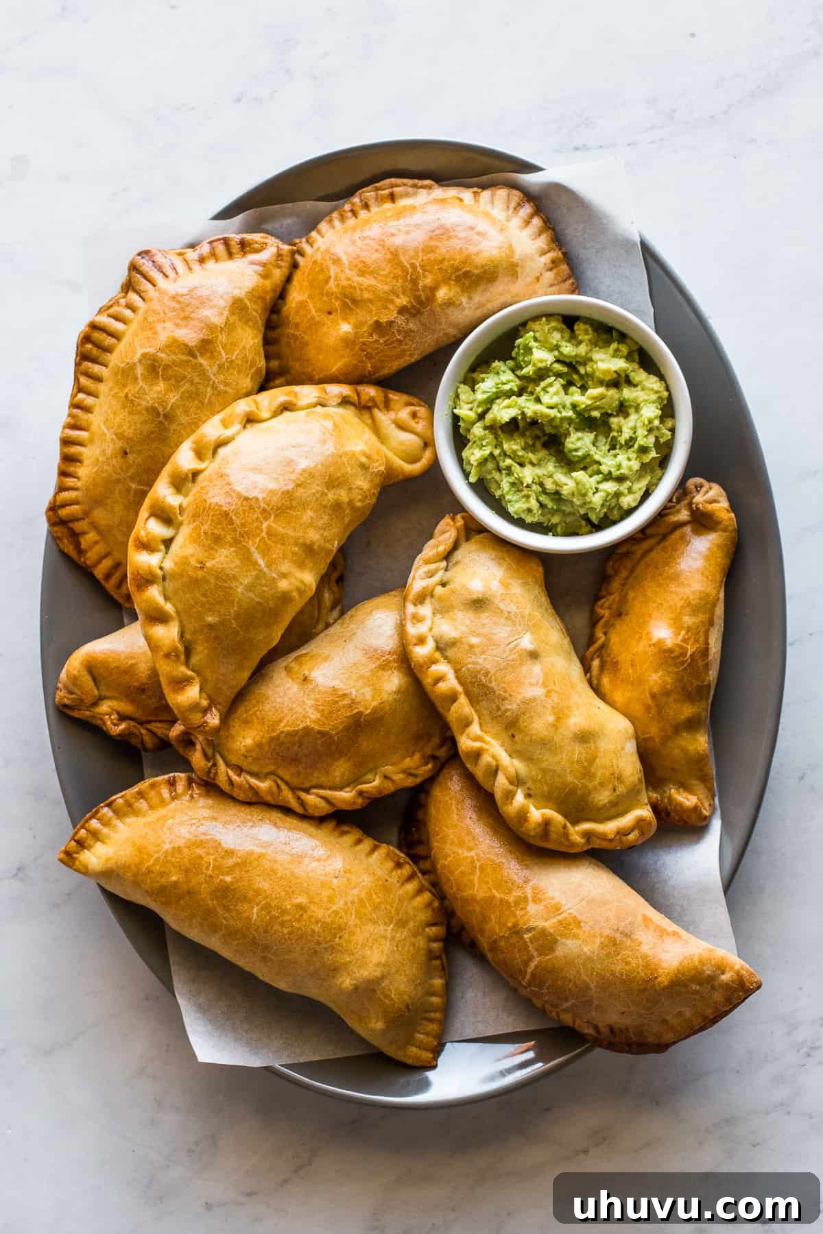 Savory Beef Pockets 2 A platter of golden brown beef empanadas, perfectly baked, with a side bowl of fresh green guacamole, ready to be enjoyed.