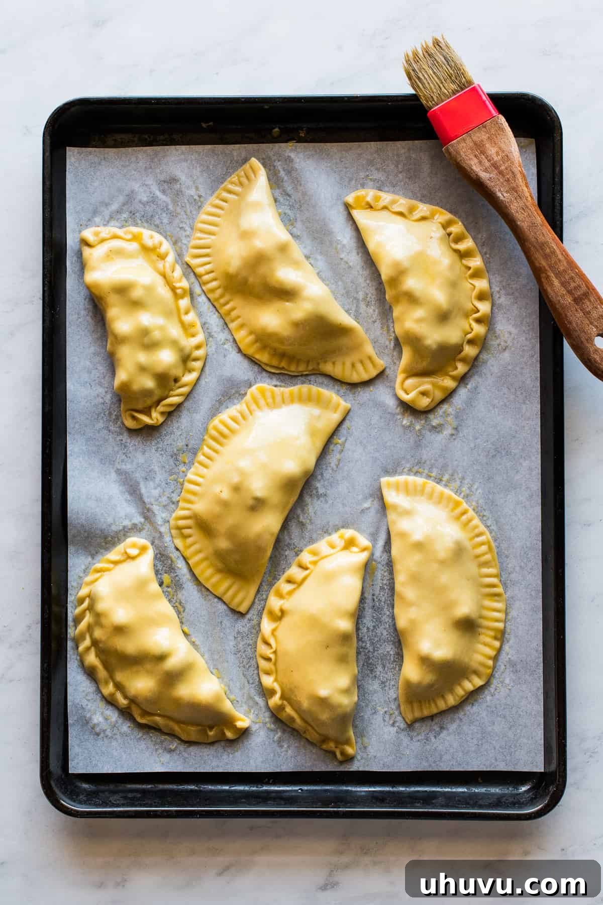 Savory Beef Pockets 8 A baking sheet lined with parchment paper, holding several neatly sealed beef empanadas, their tops brushed with egg wash, ready for baking to achieve a golden finish.