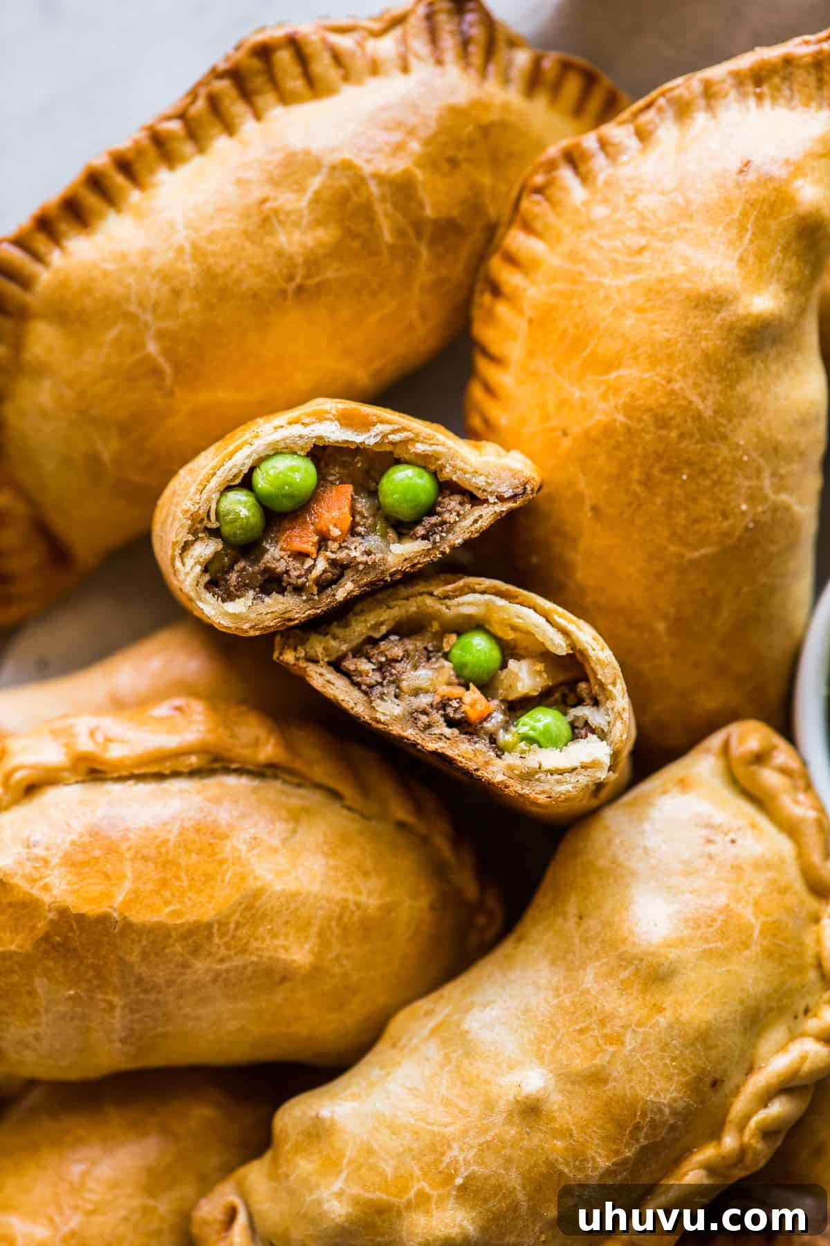 Savory Beef Pockets 9 A close-up view of a baked beef empanada cut open, revealing the delicious and savory ground beef picadillo filling with visible vegetables and melted cheese inside.