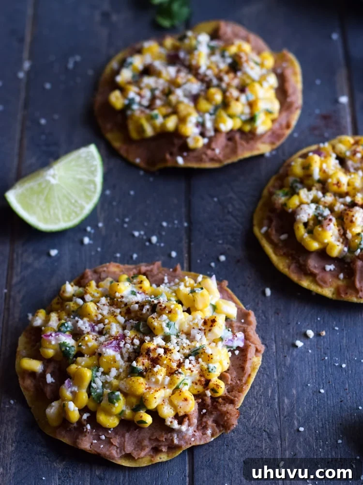Zesty Elote Tostadas 5 A vibrant Mexican Street Corn Tostada, generously topped with creamy refried beans, a colorful mixture of Mexican street corn, and crumbled Cotija cheese, resting on a wooden board. This image highlights the freshness and deliciousness of the quick, gluten-free, and vegetarian meal.