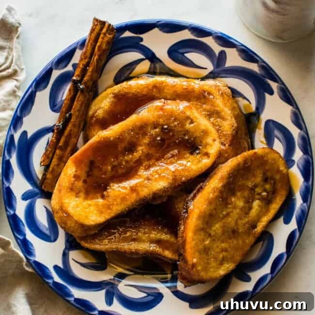 A delicious stack of Torrejas, or Mexican French Toast, drizzled with piloncillo syrup and a cinnamon stick garnish.