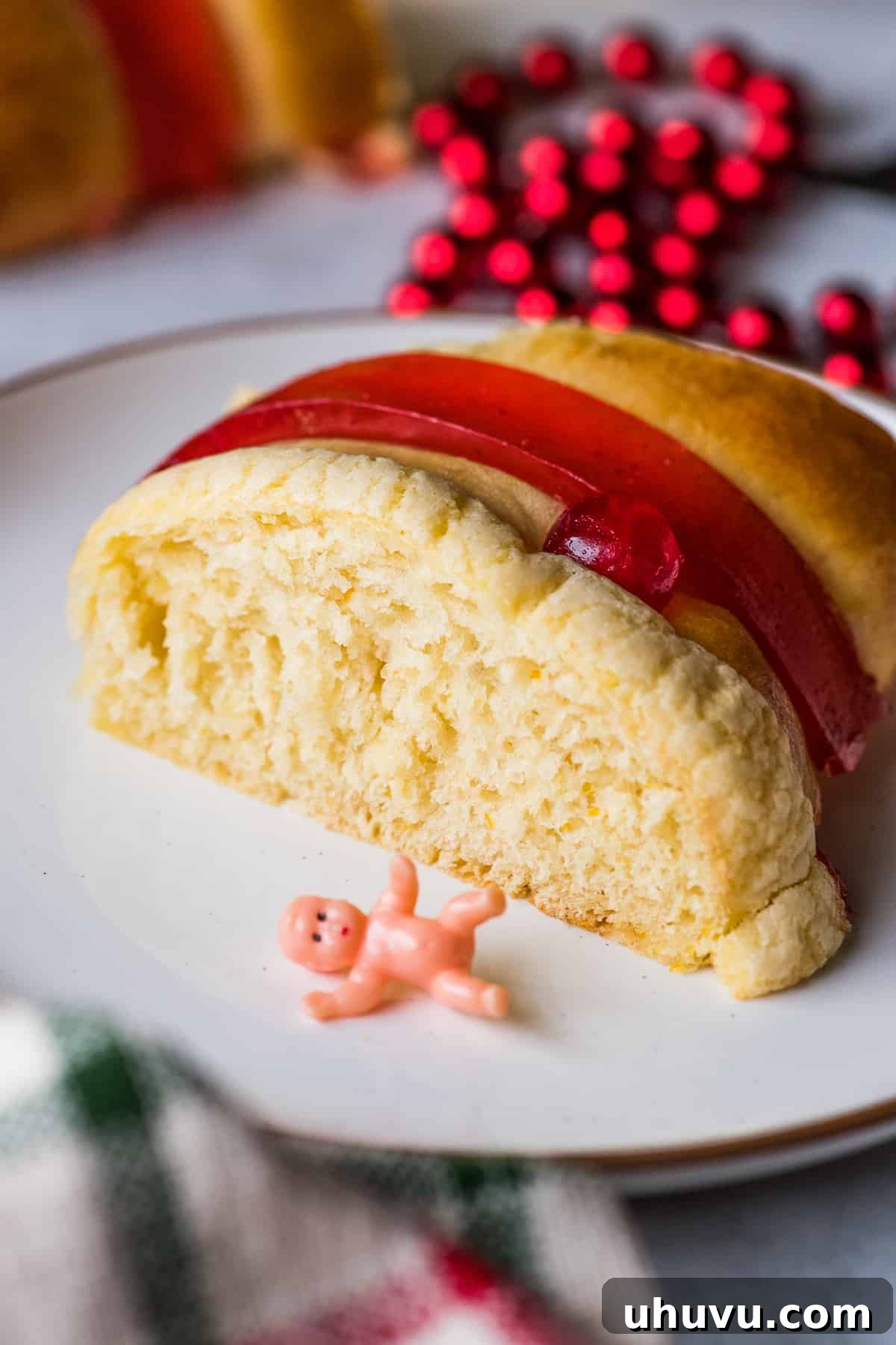 Sweet Epiphany Crown 9 A slice of Rosca de Reyes bread on a plate with a baby Jesus figurine next to it.