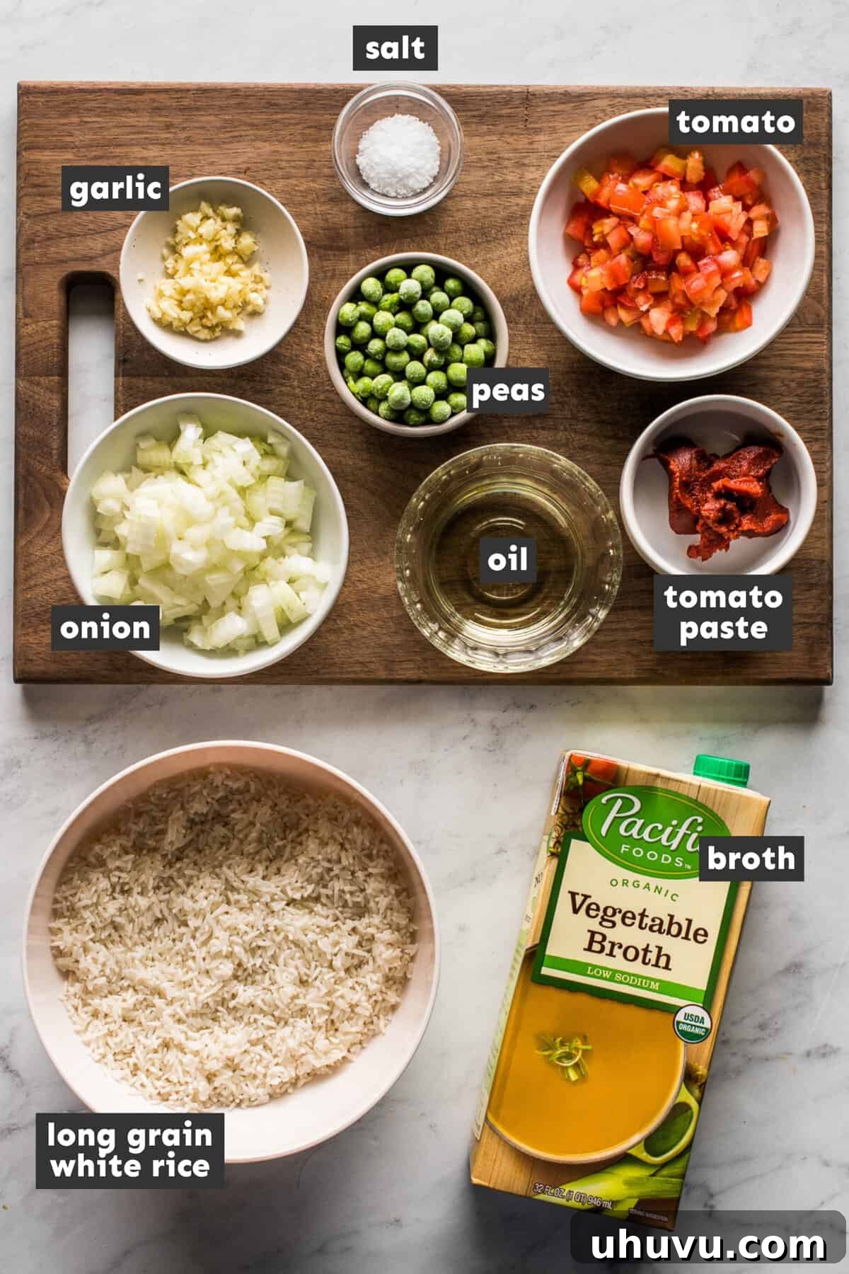 Fresh ingredients for Mexican Rice laid out on a wooden table, including long-grain white rice, roma tomatoes, onion, garlic, and frozen peas.