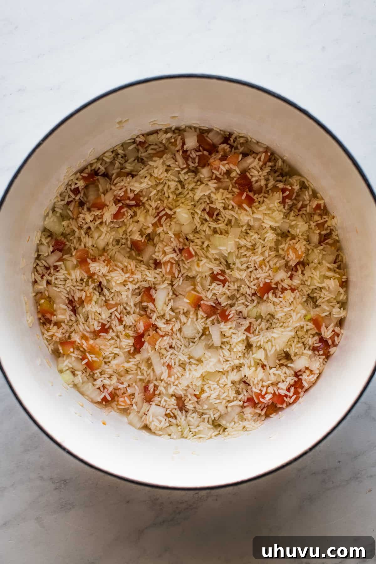 Toasted long grain white rice in a Dutch oven, now mixed with finely diced onion and tomato, ready for the next step.