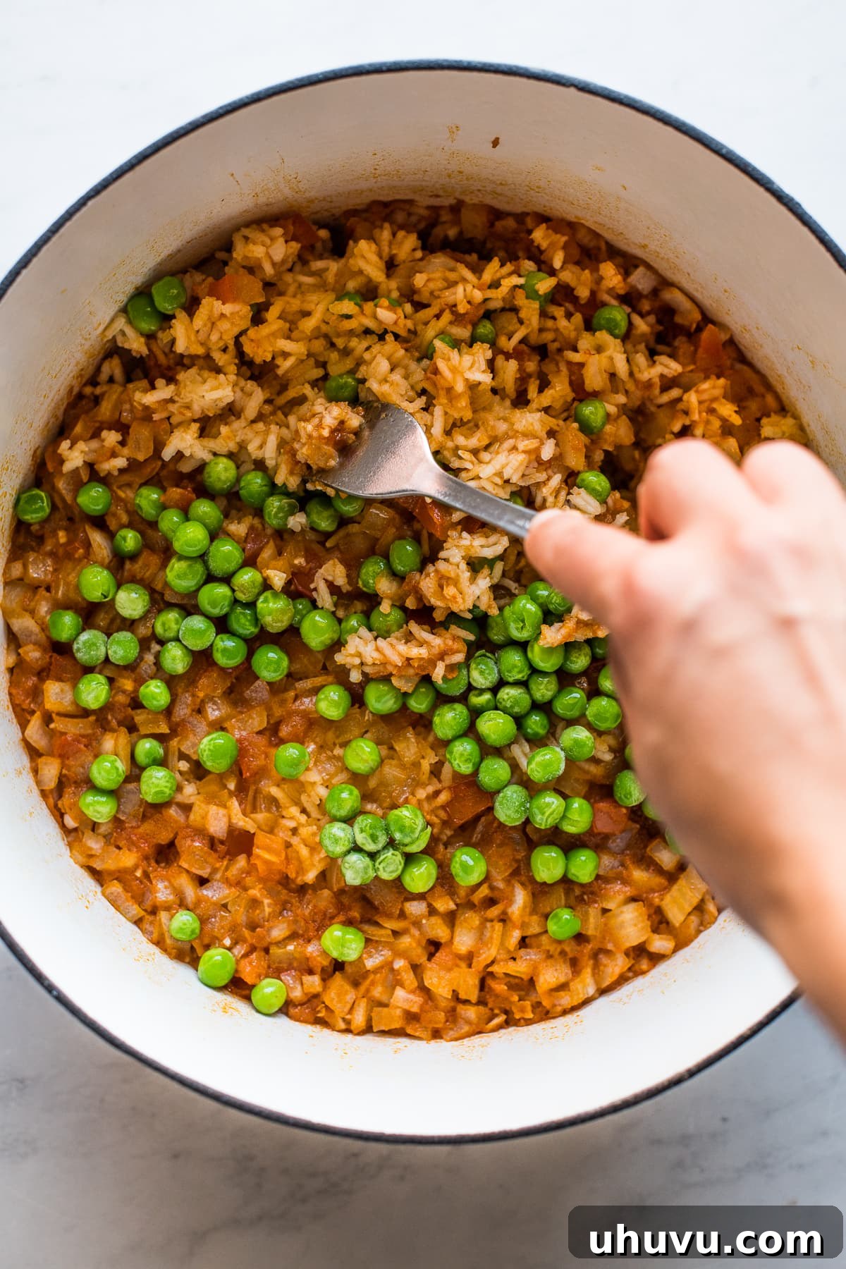 Authentic Mexican rice being gently fluffed with a fork, revealing vibrant green peas mixed throughout the fluffy red grains.