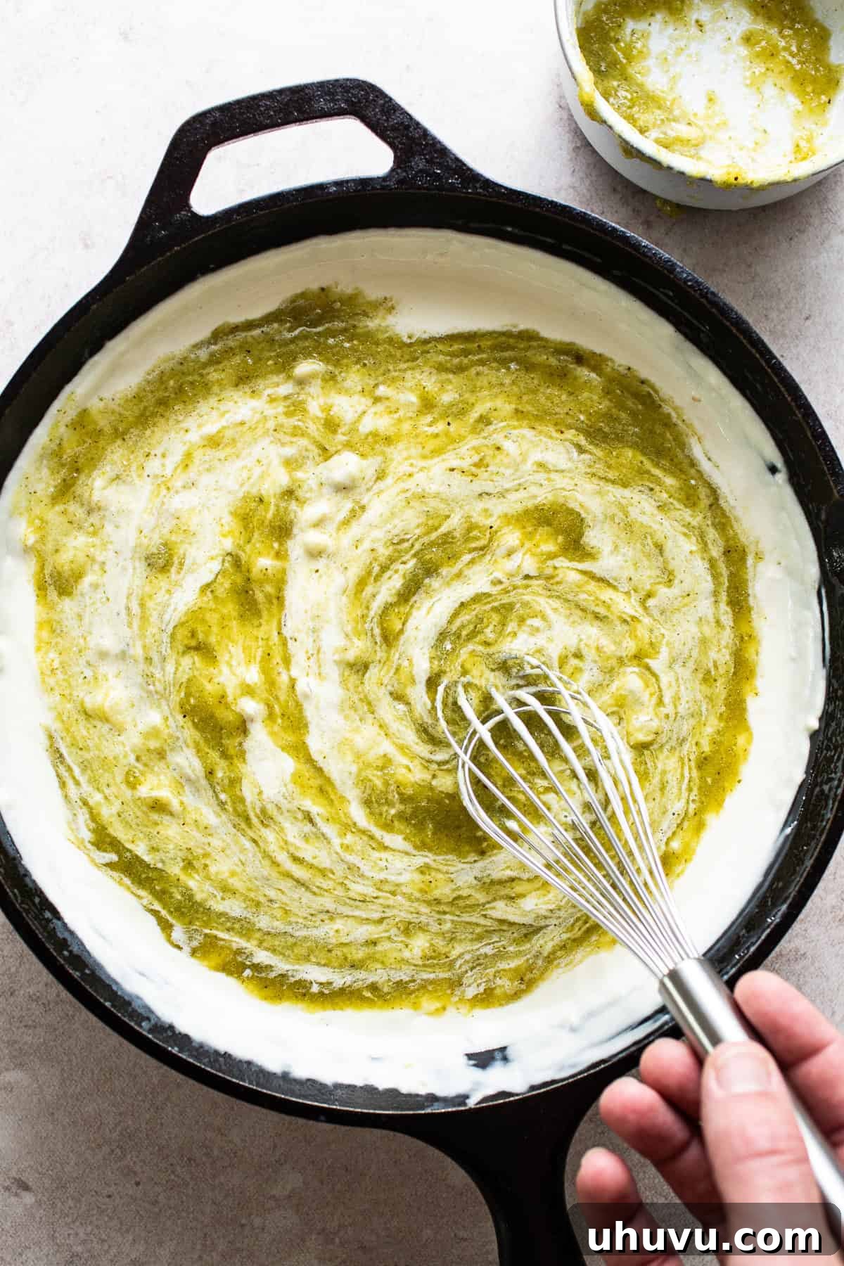 Zesty Green Chili Queso 5 Salsa verde, onions, garlic, butter, milk, and cream cheese in a skillet being melted together and whisked.