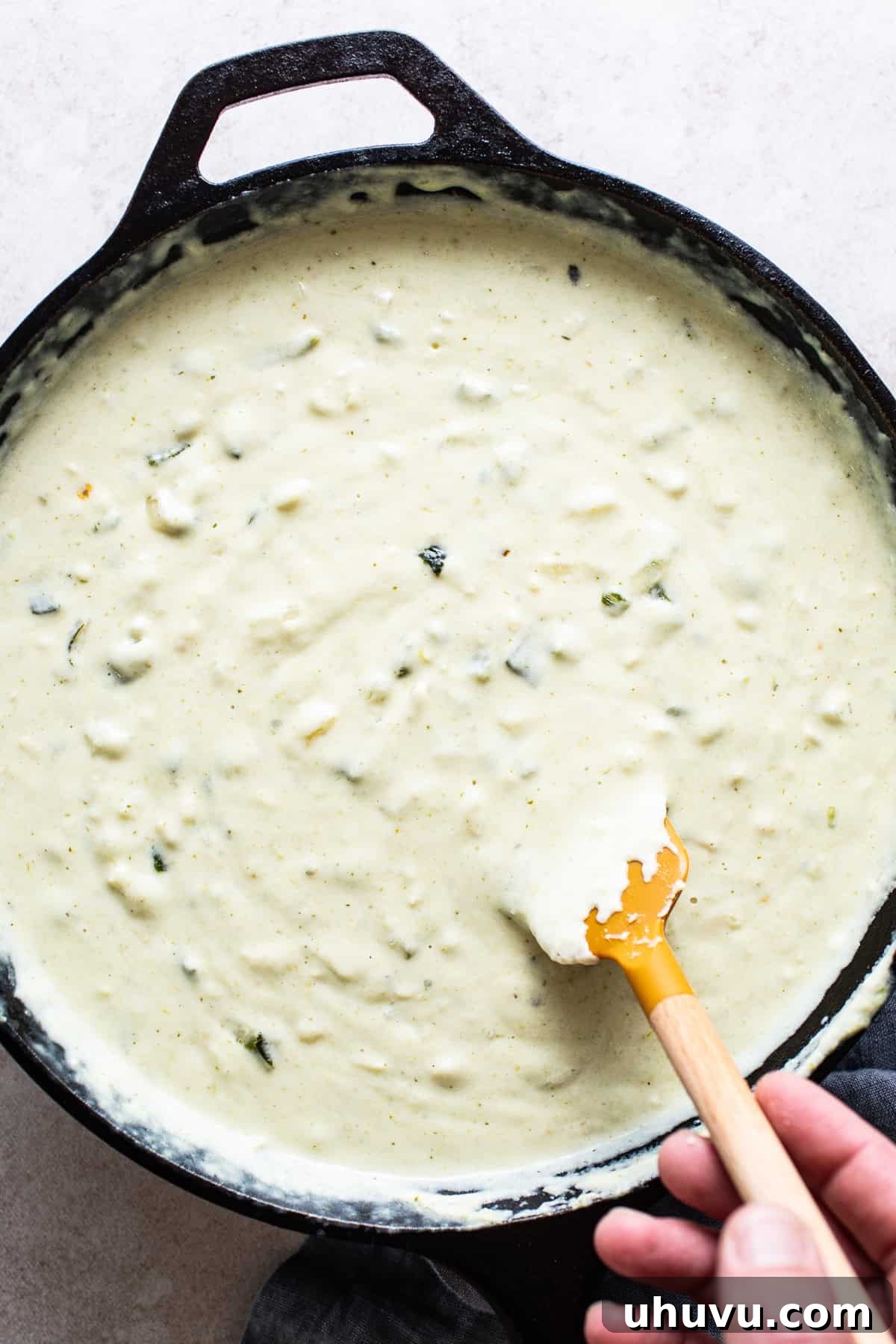 Zesty Green Chili Queso 6 Melted shredded cheese being mixed into a large skillet to make salsa verde queso.