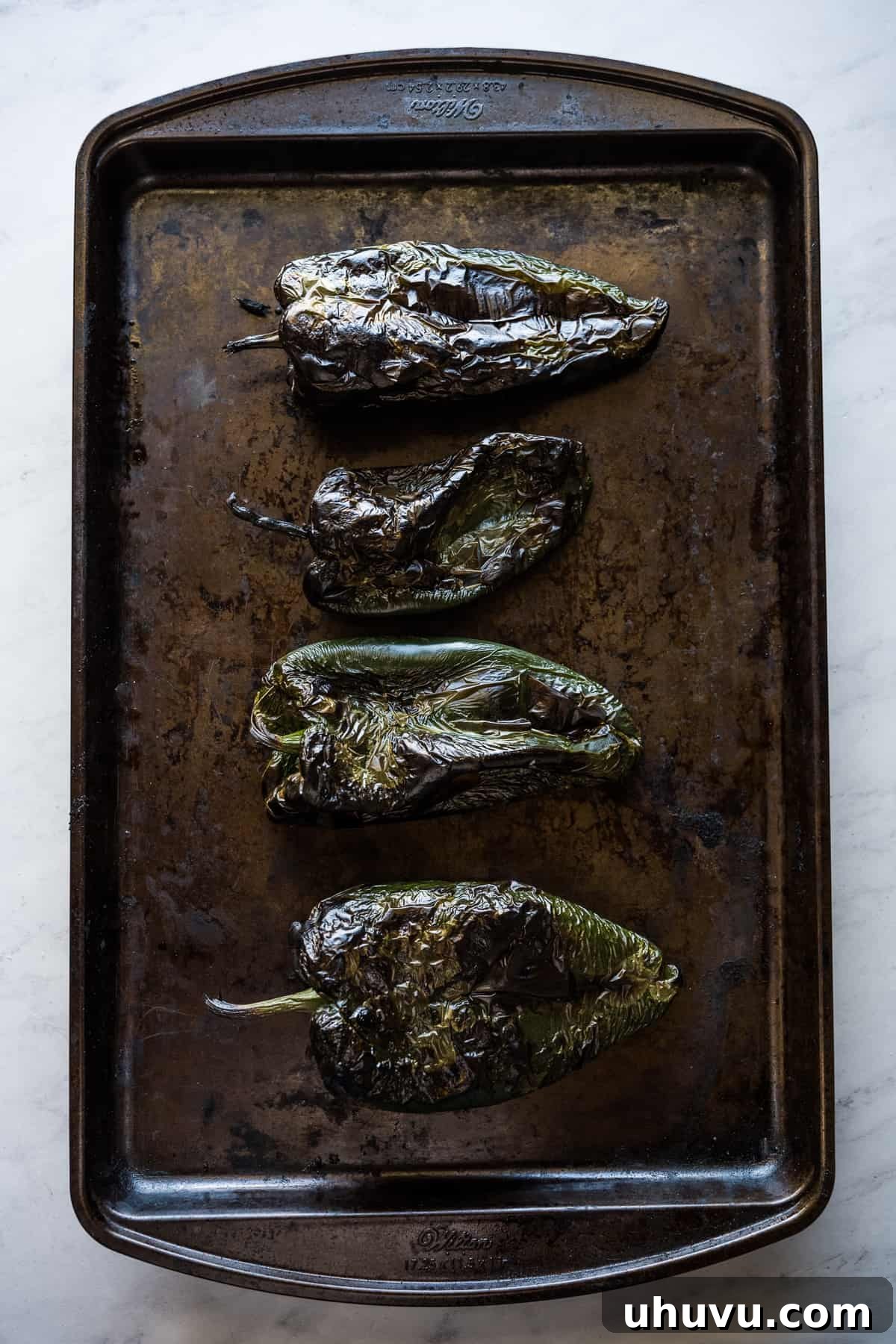 Zesty Green Spaghetti 5 Roasted poblano peppers cooling on a baking sheet, with visible charred skin.