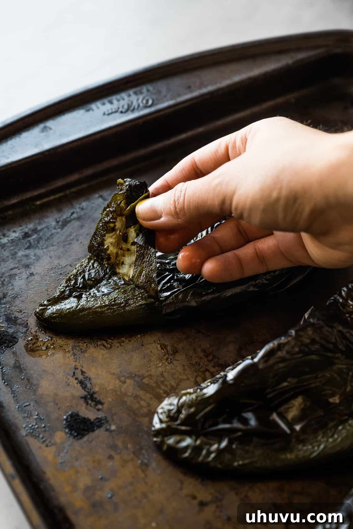 Zesty Green Spaghetti 6 A hand peeling the charred skin off a roasted poblano pepper, revealing the soft flesh underneath.