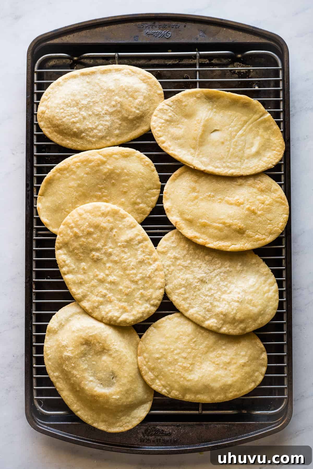 Freshly fried huaraches resting on a baking sheet lined with paper towels, allowing excess oil to drain and leaving them perfectly crispy.