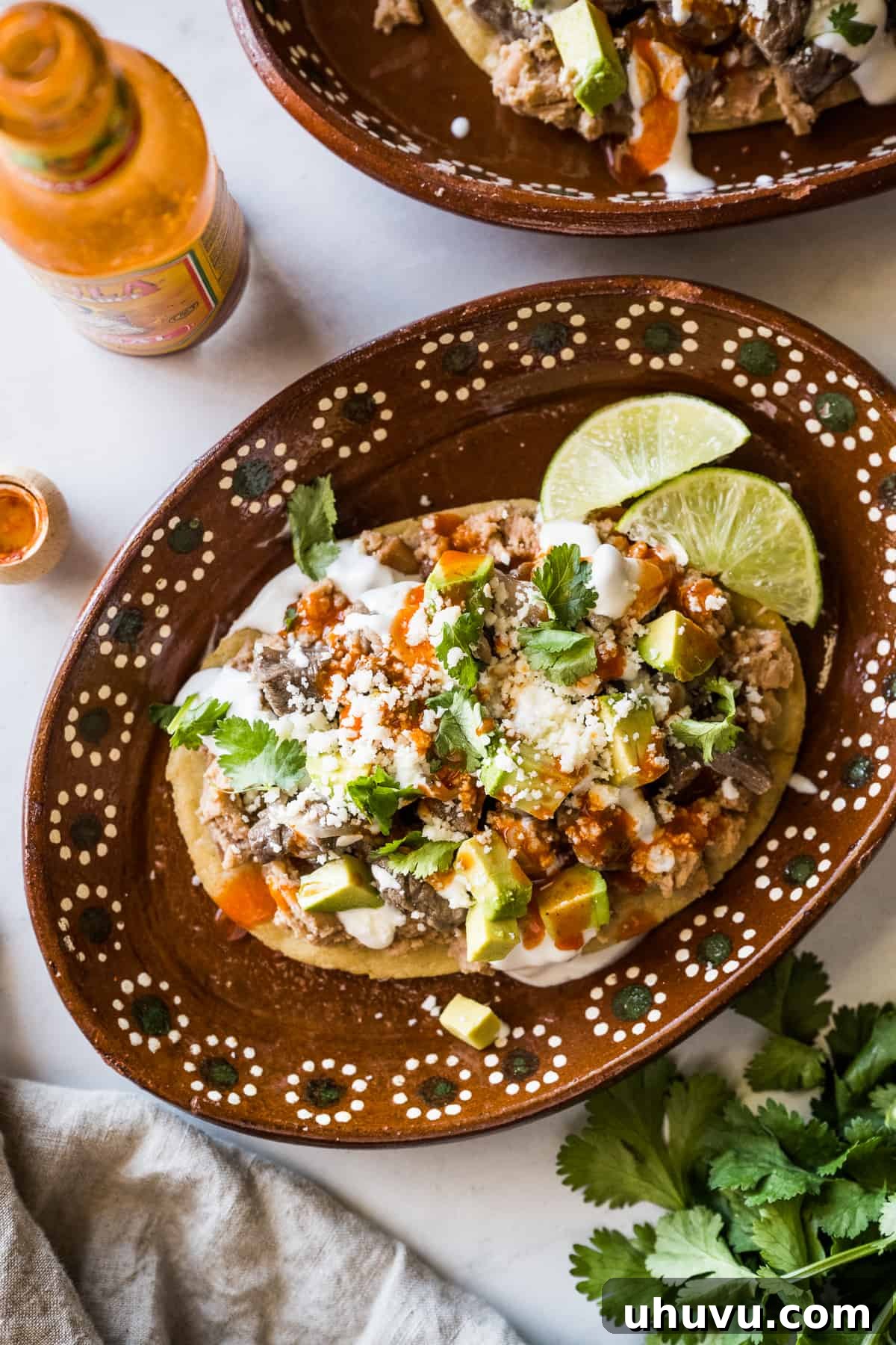 A beautifully plated Mexican huarache, generously topped with refried beans, savory beef, fresh onions, and a variety of colorful garnishes.