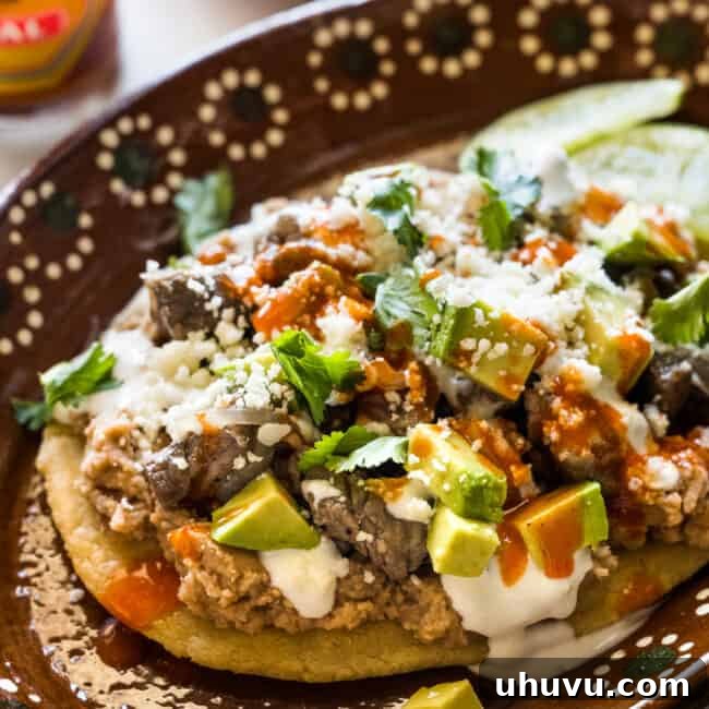 A delicious Mexican Huarache on a plate topped with creamy refried beans, crumbled cheese, and other fresh garnishes.