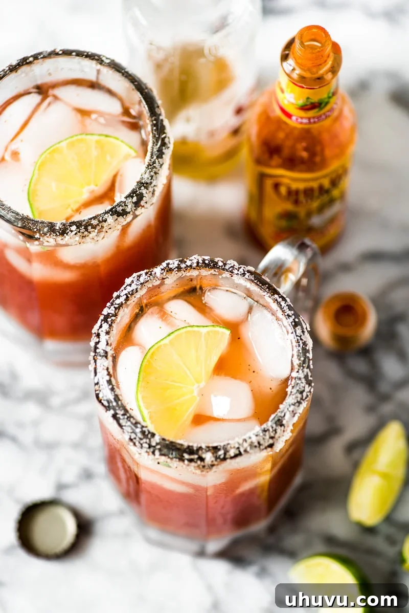 The Ultimate Michelada 4 Two micheladas in beer pint glasses topped with lime wedges next to hot sauce bottles.