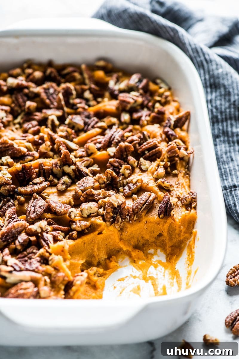 A healthy sweet potato casserole in a white baking dish topped with candied pecans.