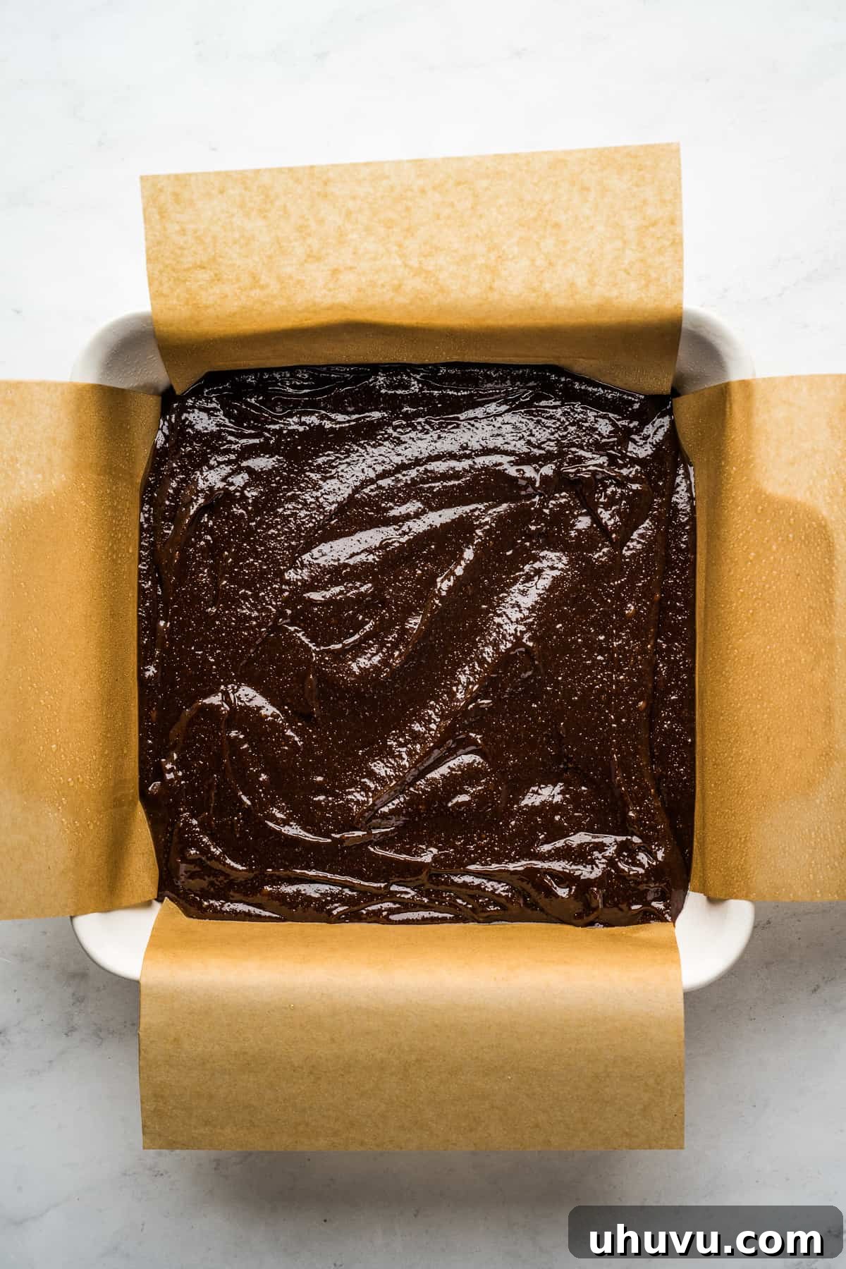 Brownie batter in a square baking pan lined with parchment paper