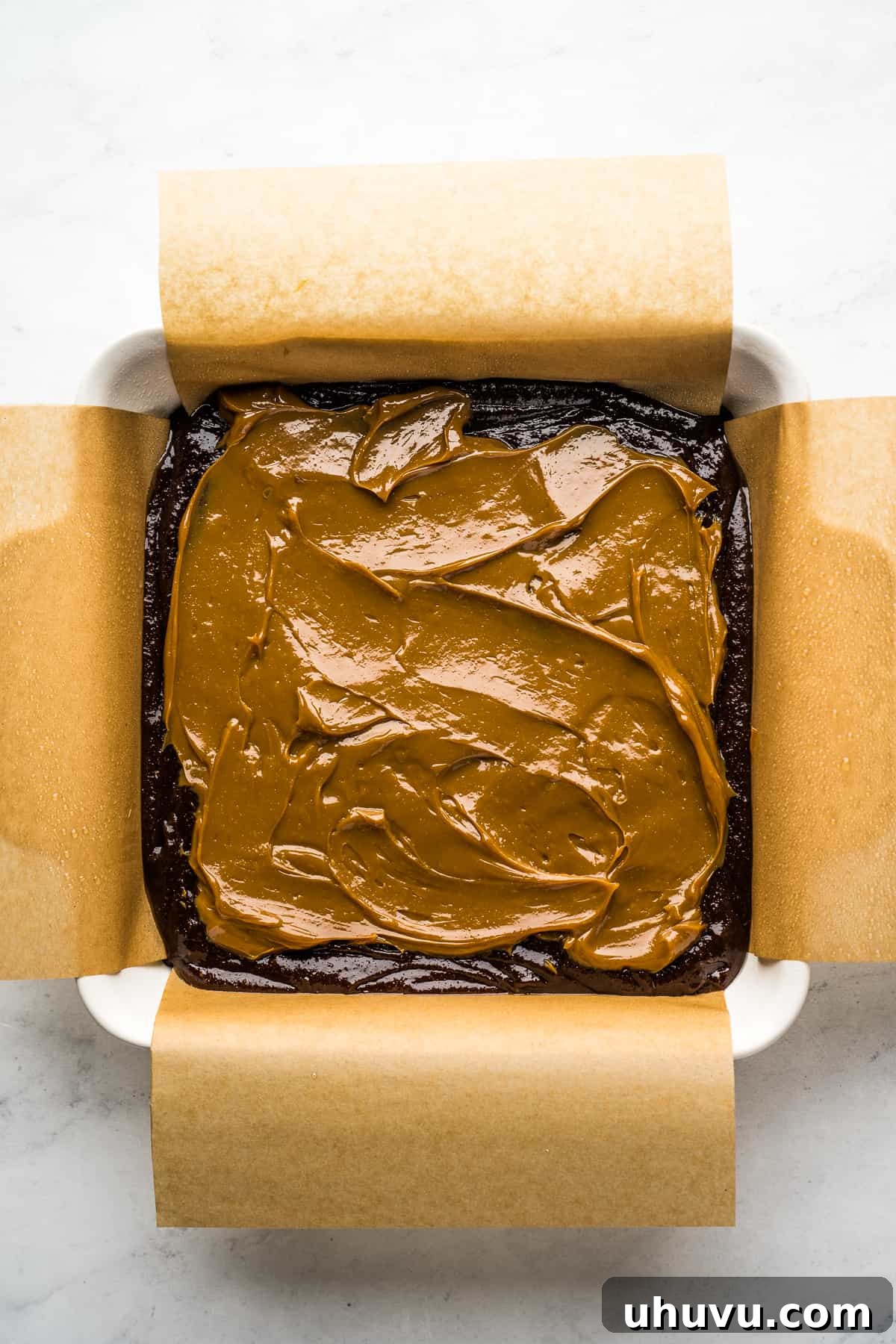 Brownie batter topped with a layer of dulce de leche on top in a square baking pan