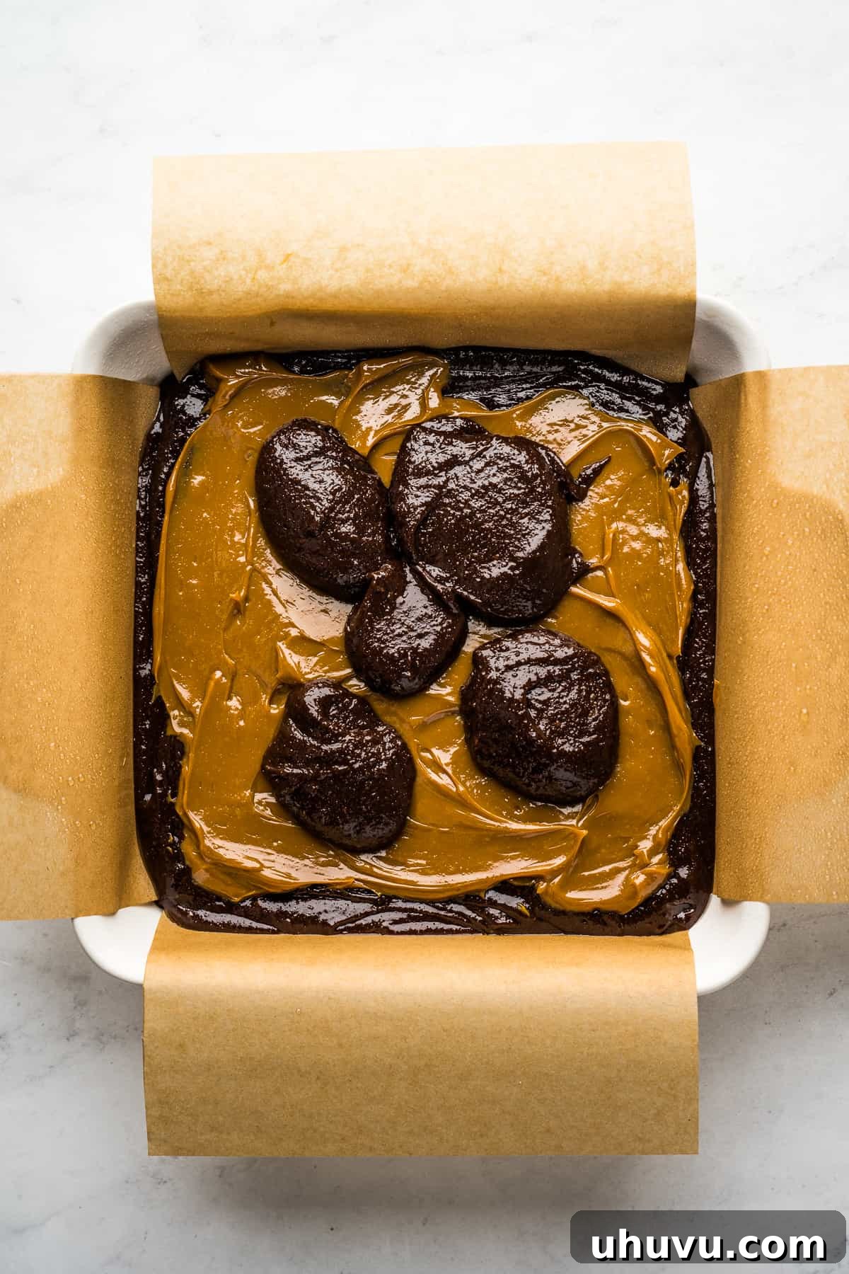 Brownie batter in a baking dish topped with a layer of dulce de leche and another layer of brownie batter on top
