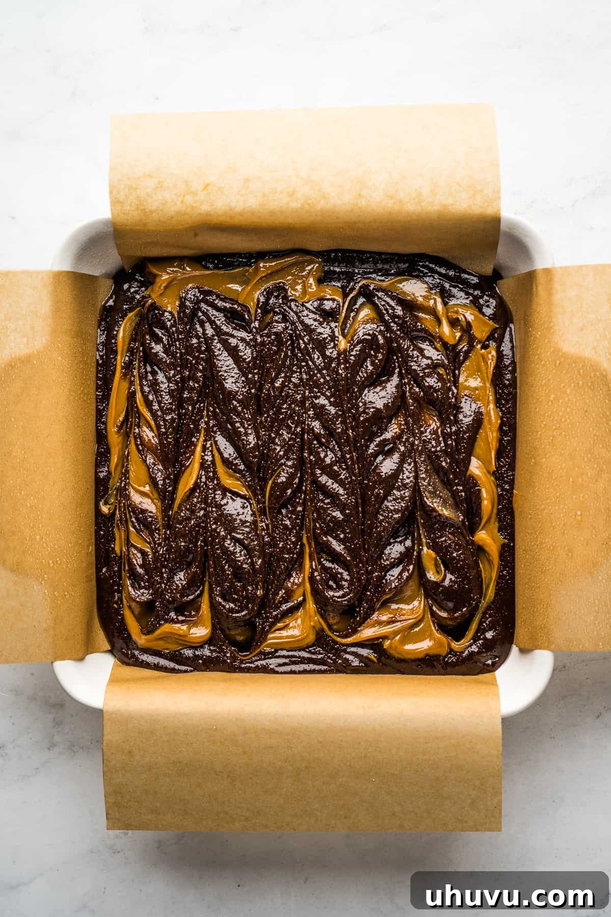 Dulce de leche brownie batter in a square baking dish lined with parchment paper