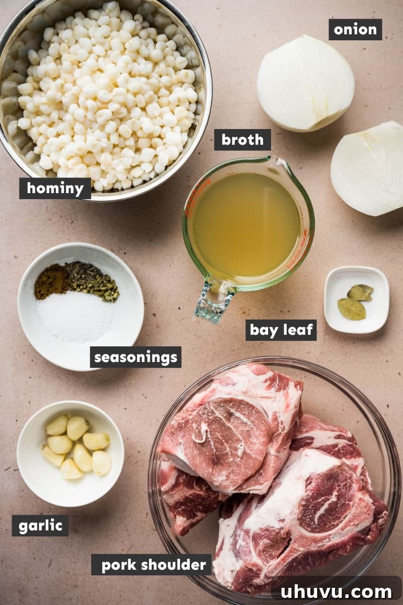 A collection of fresh ingredients for Pozole Blanco arranged on a rustic wooden table, including a large pork shoulder, cans of white hominy, onions, garlic, bay leaves, and a selection of dried spices.