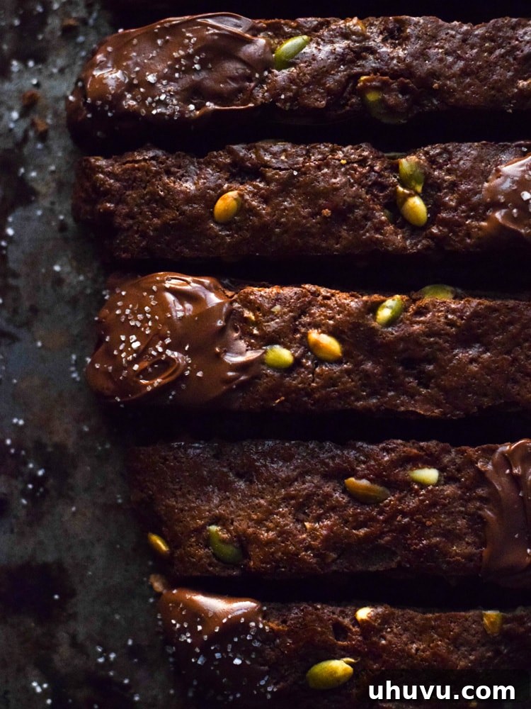 Crisp Cocoa Pepita Biscotti 4 Artfully arranged Mexican Chocolate Pumpkin Seed Biscotti on a baking sheet, with some pieces dipped in chocolate and sea salt, exuding holiday perfection and inviting warmth.