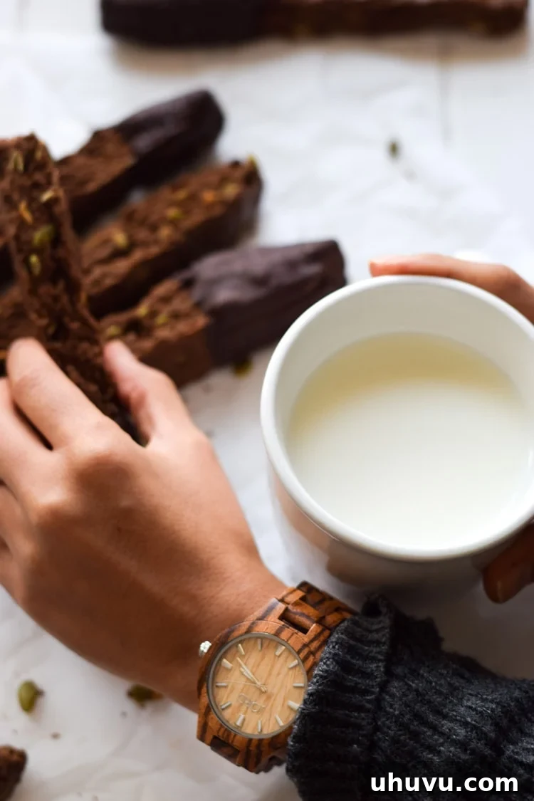 Crisp Cocoa Pepita Biscotti 6 Hand holding a Mexican Chocolate Pumpkin Seed Biscotti, dipped in chocolate and sea salt, with a JORD Wood Watch in the background, embodying holiday perfection and thoughtful gifting.