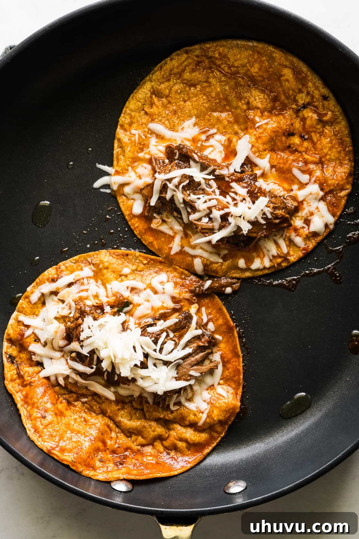 Birria tacos frying in a skillet.