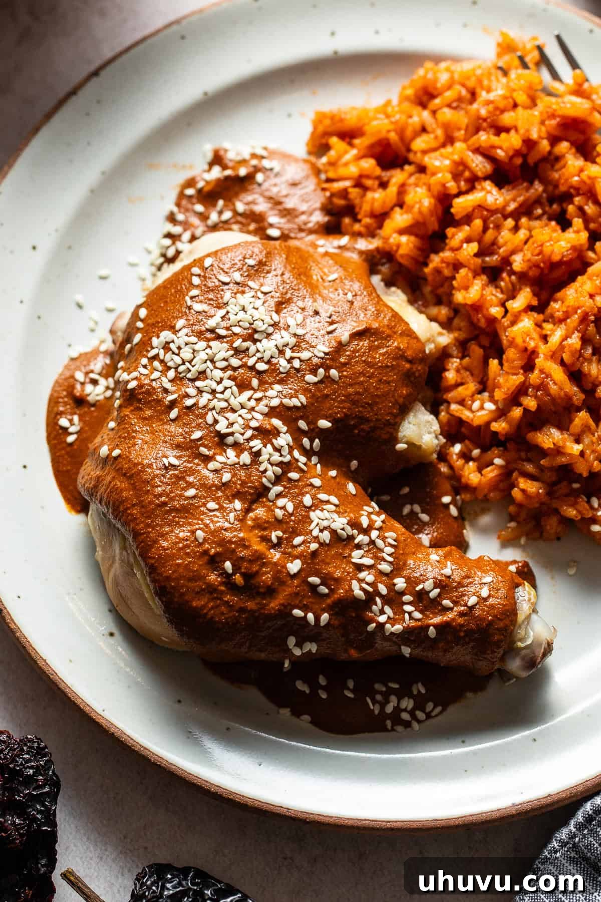 Classic Mexican Mole Poblano Sauce 10 A cooked chicken leg quarter generously spooned with Mole Poblano sauce and garnished with white sesame seeds on a plate.