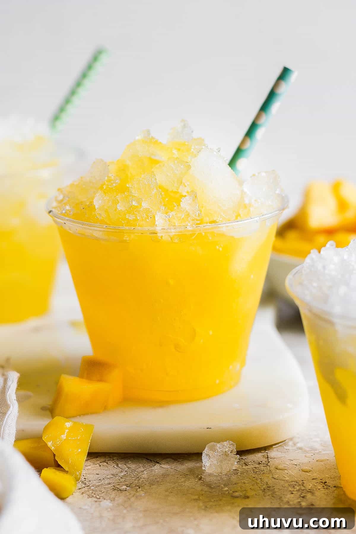 A vibrant cup of Mexican Raspados, featuring finely shaved ice generously topped with a rich, sweet mango syrup and garnished with fresh mango chunks and a straw. Perfect for a refreshing summer treat.