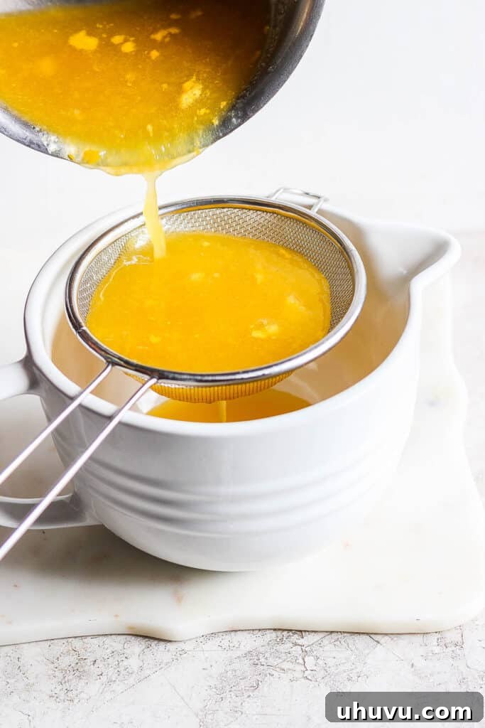 Thick mango syrup being poured through a fine-mesh strainer into a bowl, ensuring a smooth consistency for delicious raspados.