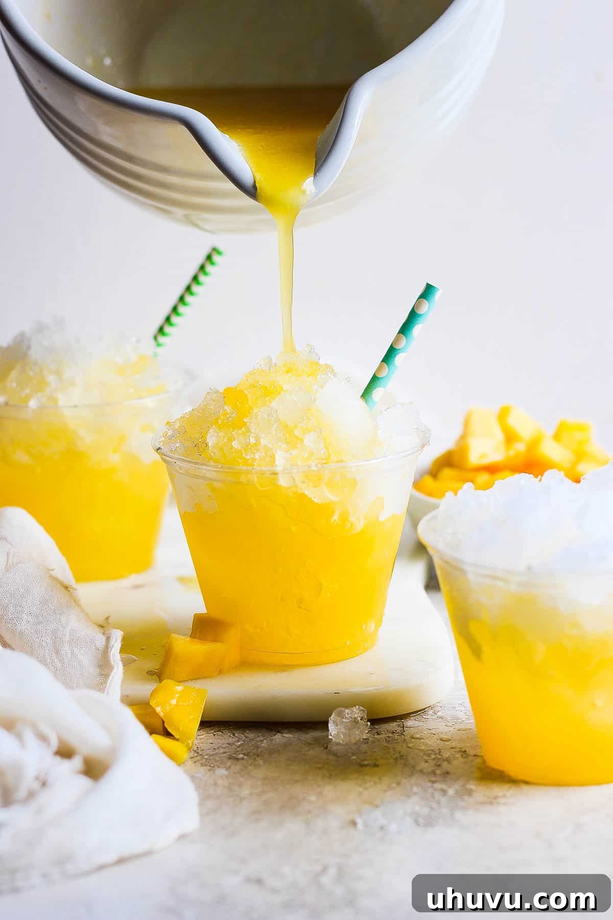 Close-up of mango syrup being poured over finely shaved ice packed into a clear plastic cup, ready to be served as a refreshing Mexican Raspado.