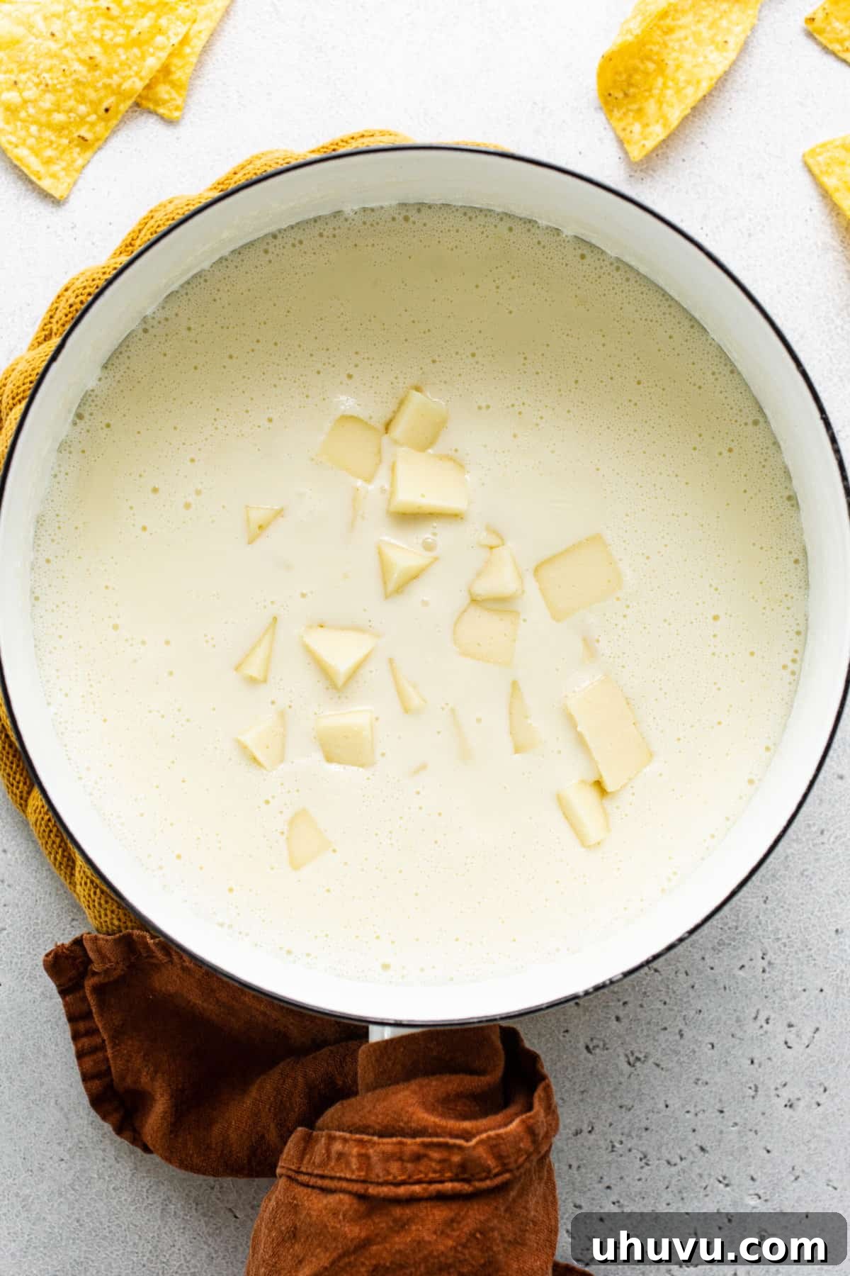 Pure White Cheese 4 Small cubes of white American cheese are being carefully added to a pot of warm milk on the stovetop, ready to be melted into a smooth queso blanco.