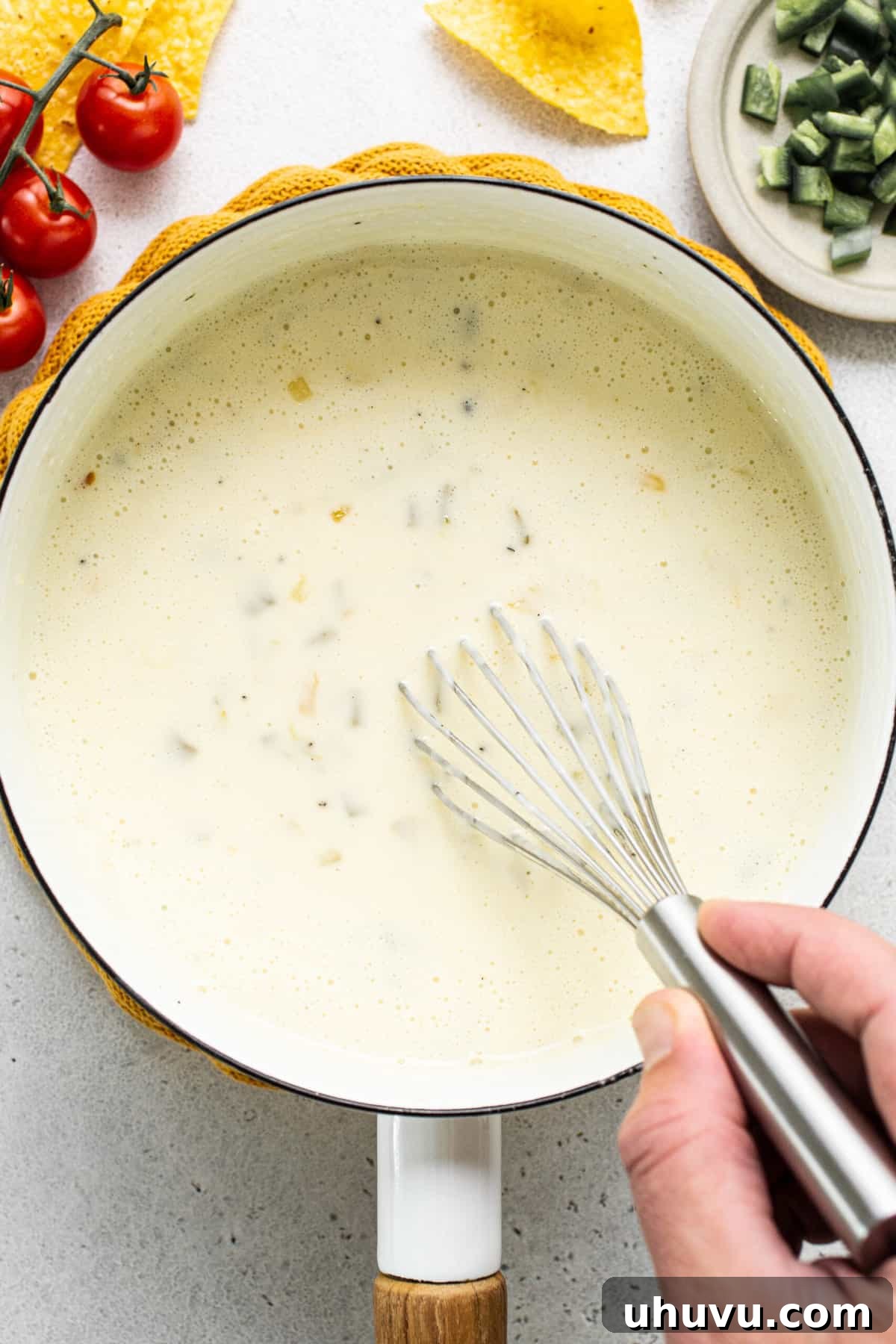 Pure White Cheese 5 A hand is actively whisking a pot of perfectly melted queso blanco on the stovetop, ensuring a smooth and creamy consistency.