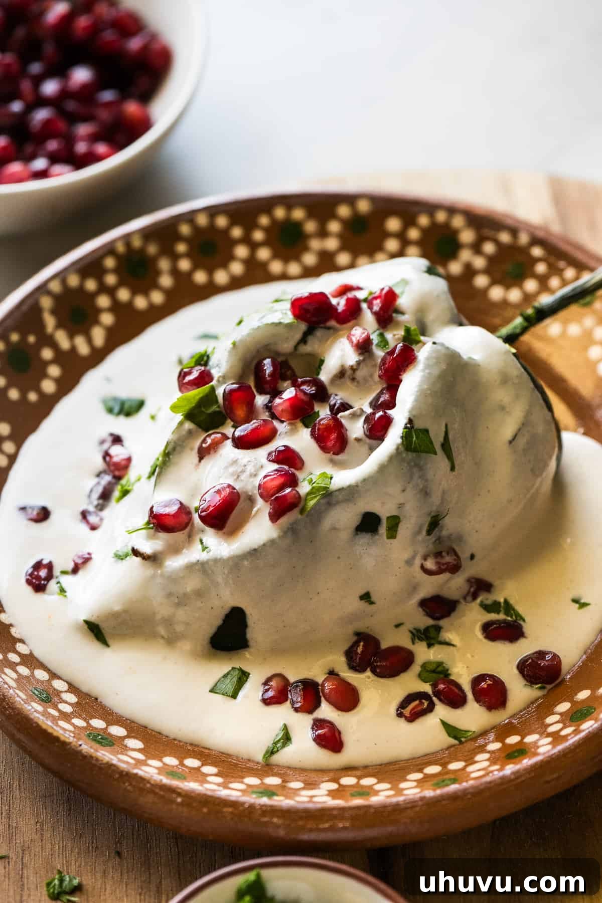 A chile en nogada on a plate garnished with pomegranate seeds and parsley.
