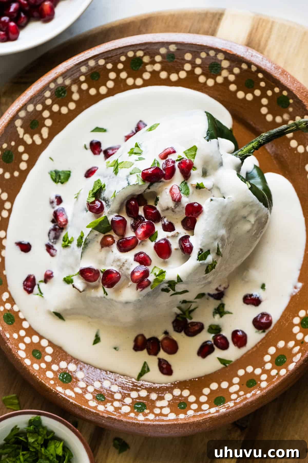Mexican chiles en nogada topped with a walnut sauce and garnished with pomegranate seeds and chopped parsley.