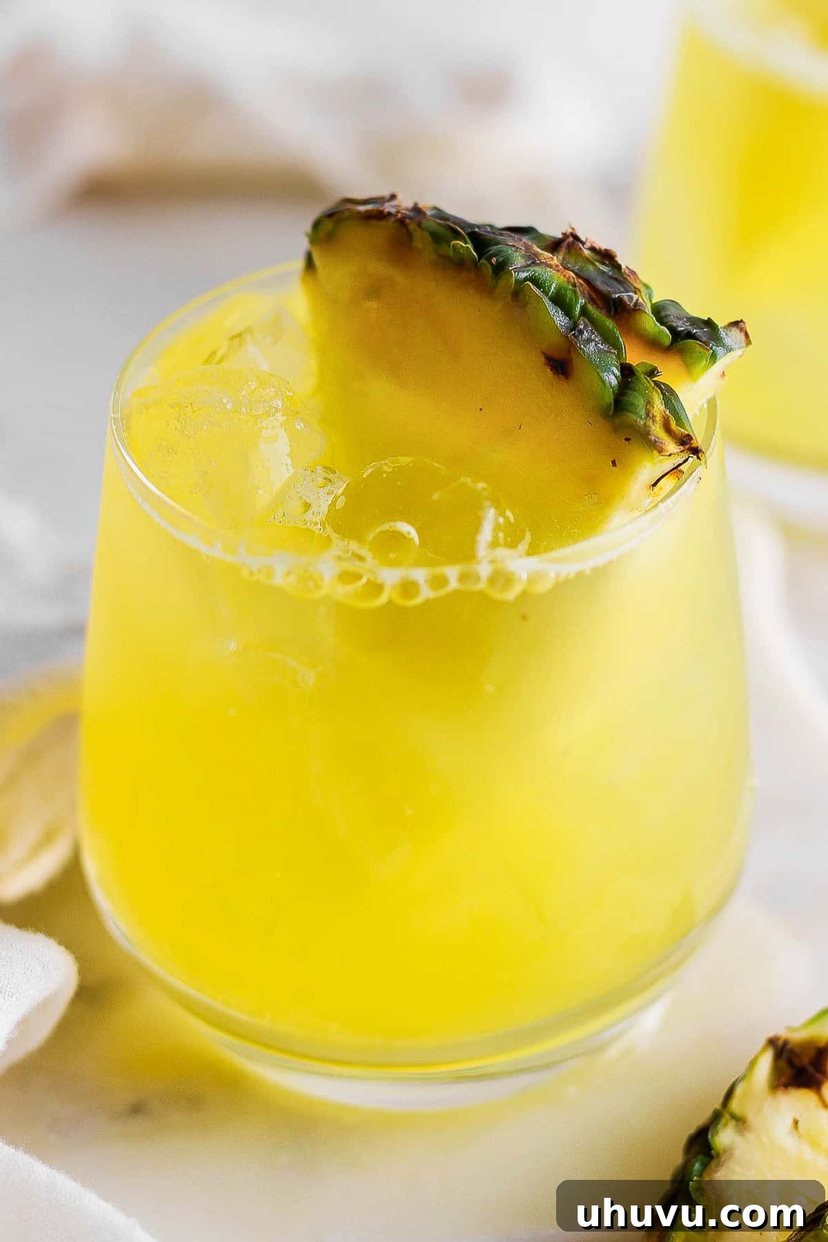 Tropical Pineapple Quencher 8 Agua de pina in a glass with ice garnished with a pineapple wedge.