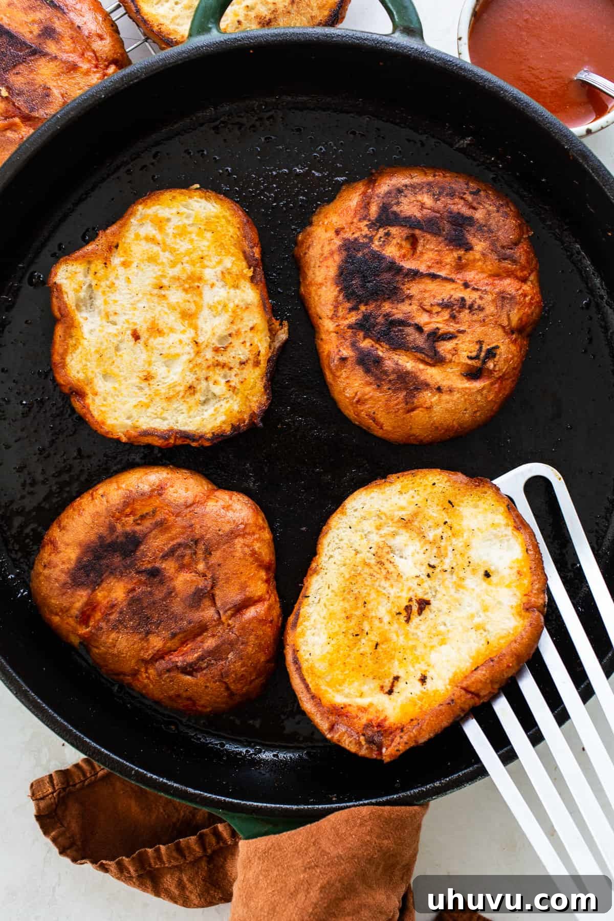 Telera bread being pan-fried in a skillet with a red chile sauce.