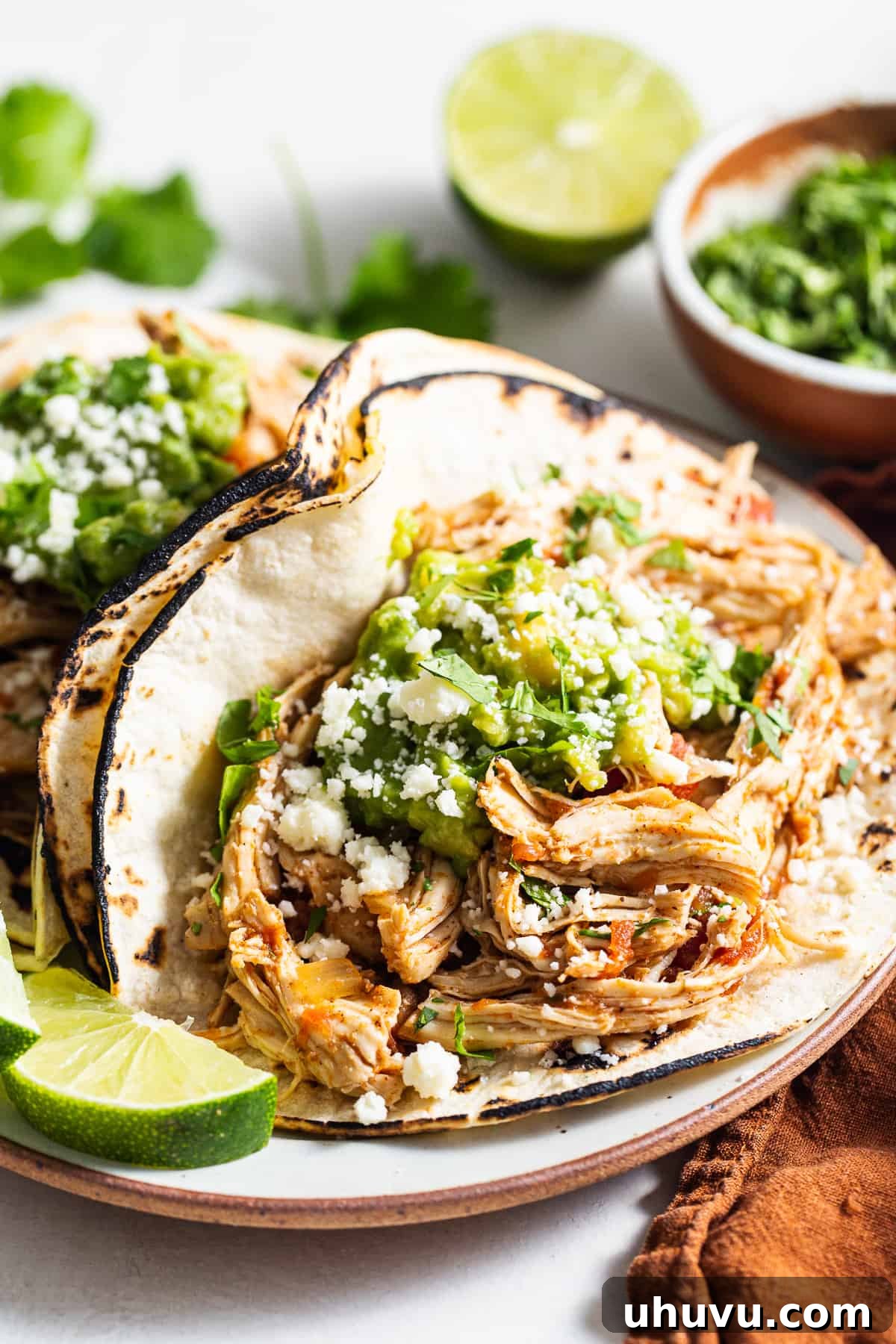 Crockpot chicken tacos served with fresh guacamole, cotija cheese, and lime wedges.