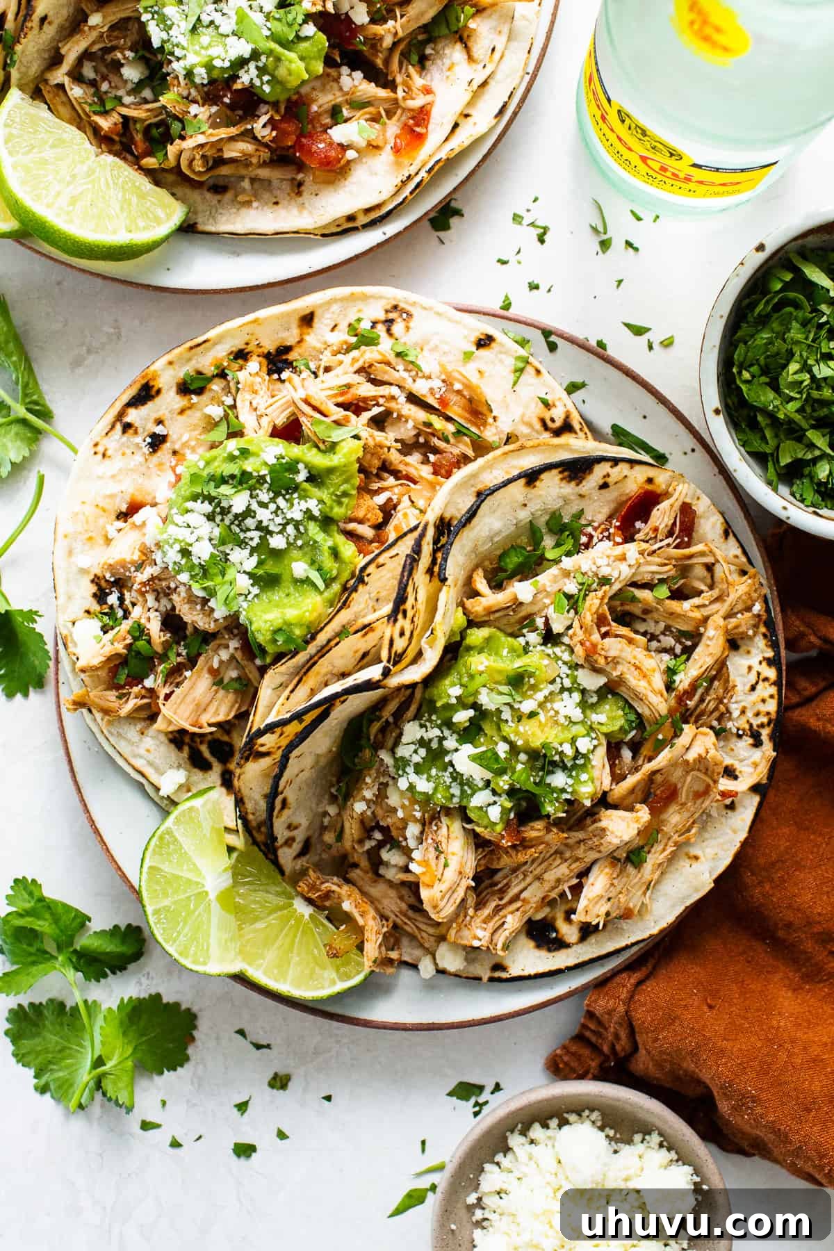 Crockpot Chicken Tacos served on a plate with fresh toppings and lime wedges.