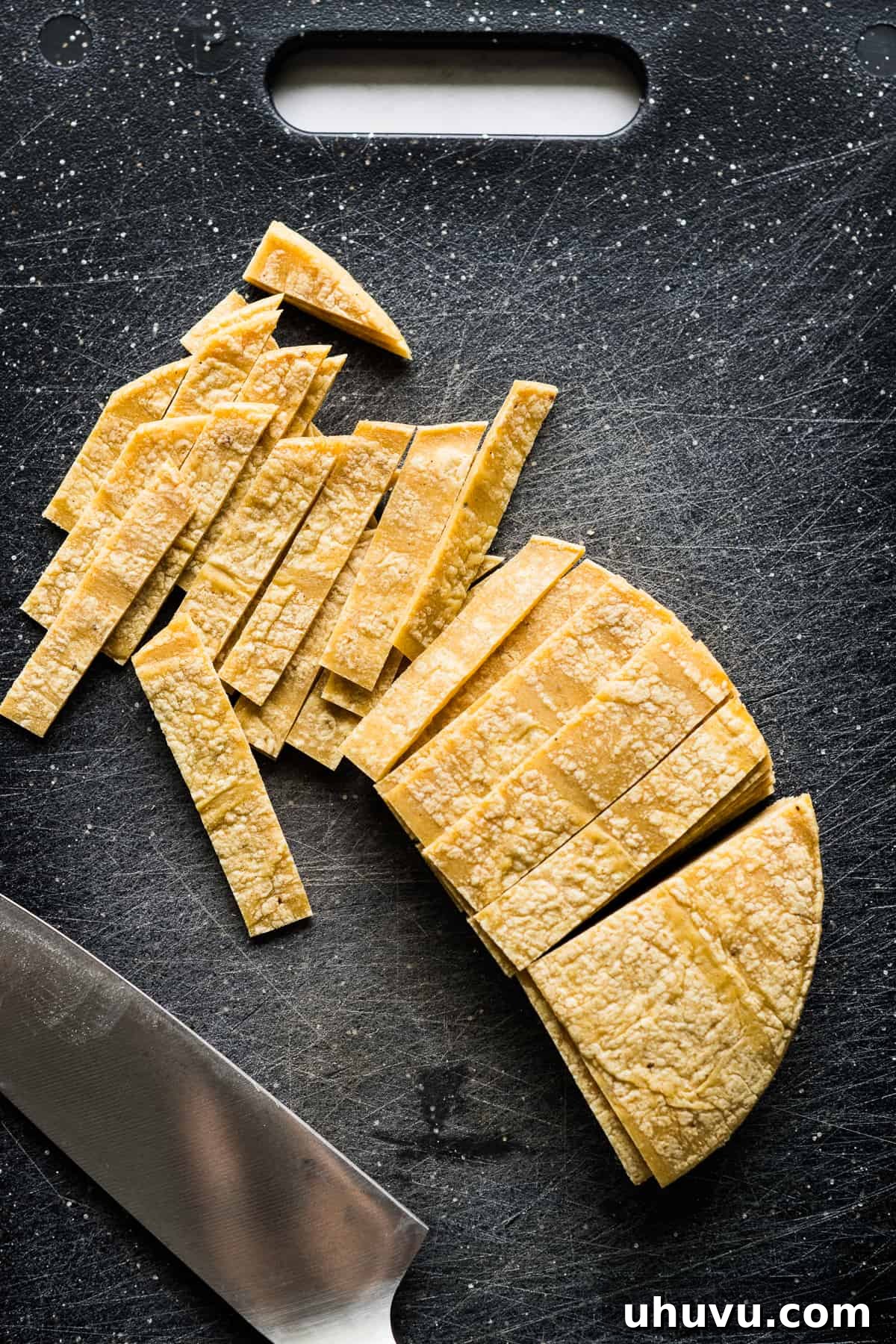 Tortilla Crisps 5 Corn tortillas precisely sliced into uniform 1/2-inch strips on a cutting board, ready for frying or baking.