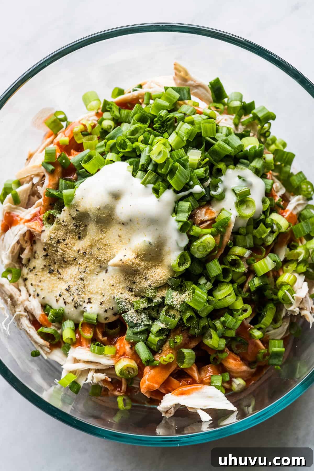 Zesty Buffalo Chicken Melts 4 Shredded chicken, buffalo sauce, green onions, and ranch dressing being mixed in a bowl.