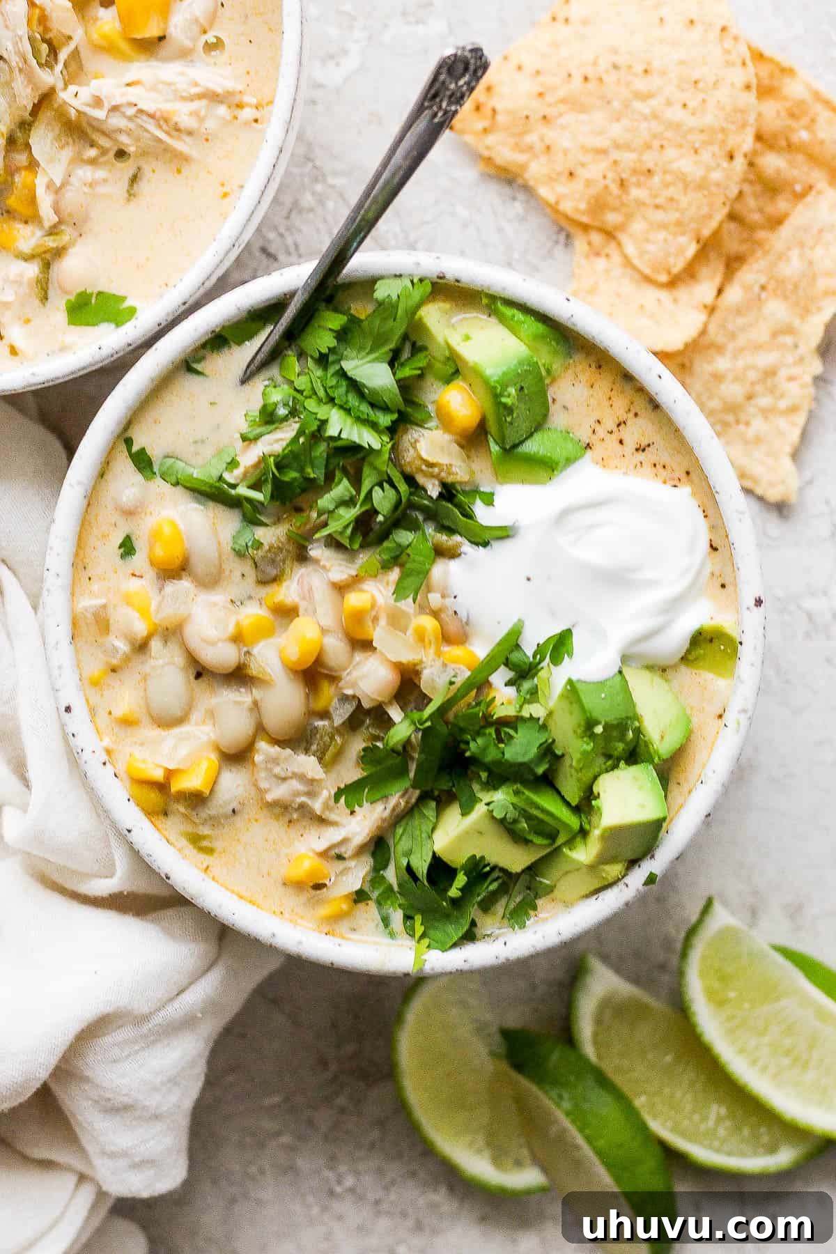 A steaming bowl of white chicken chili, richly garnished with fresh cilantro, creamy avocado slices, and a dollop of sour cream, promising a comforting and flavorful meal.