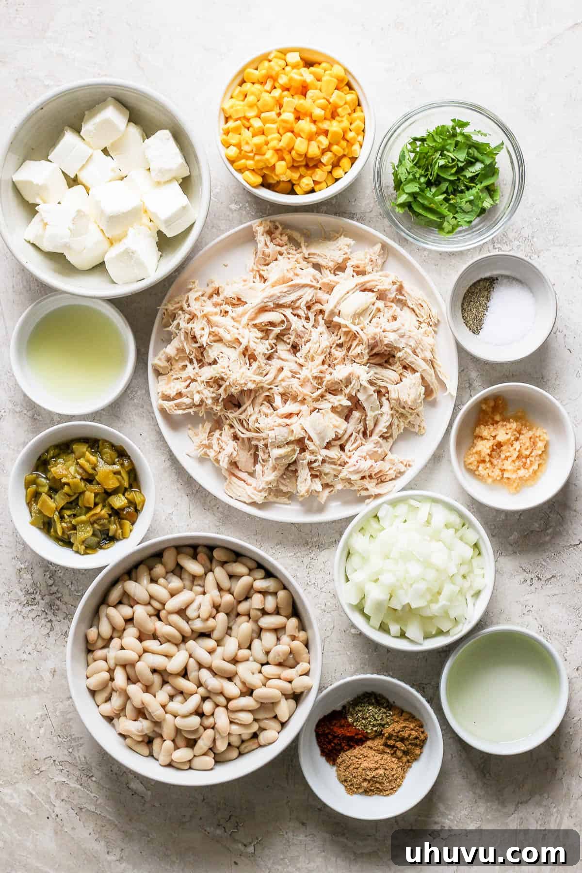 A vibrant array of fresh and canned ingredients for white chicken chili meticulously laid out on a rustic wooden table, including beans, corn, chicken, cream cheese, and various spices.