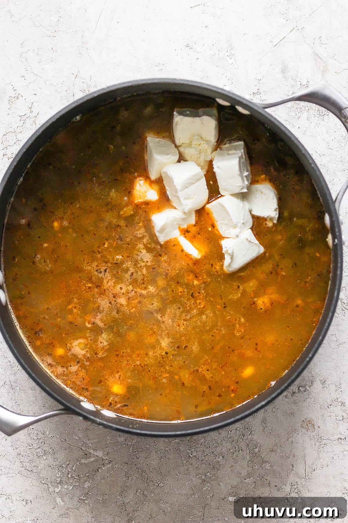 Cubes of cream cheese slowly melting into the simmering white chicken chili, creating a rich and creamy texture as it's gently stirred.