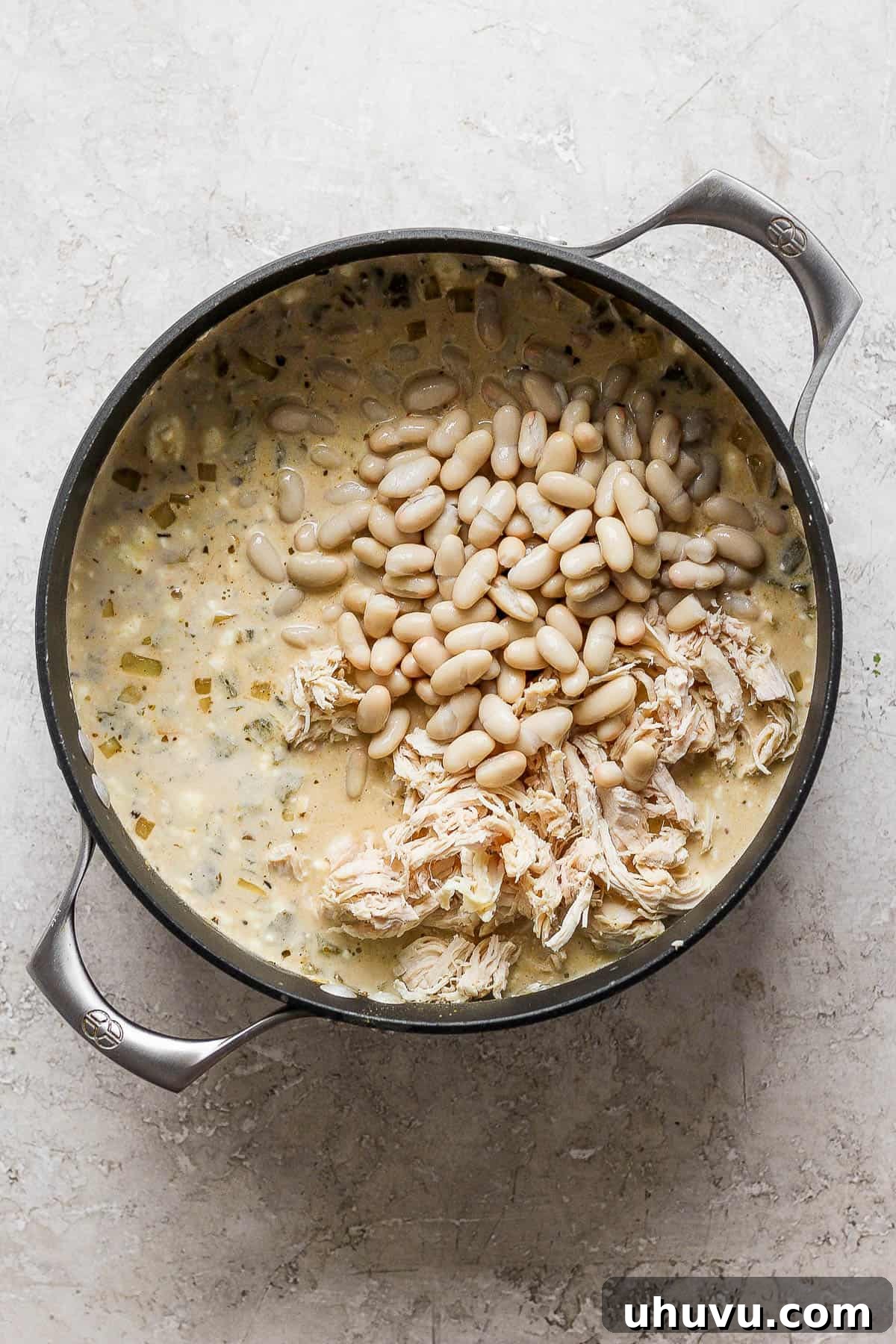 Whole cannellini beans being gently stirred into the pot of white chicken chili, adding heartiness and a pleasant texture contrast.
