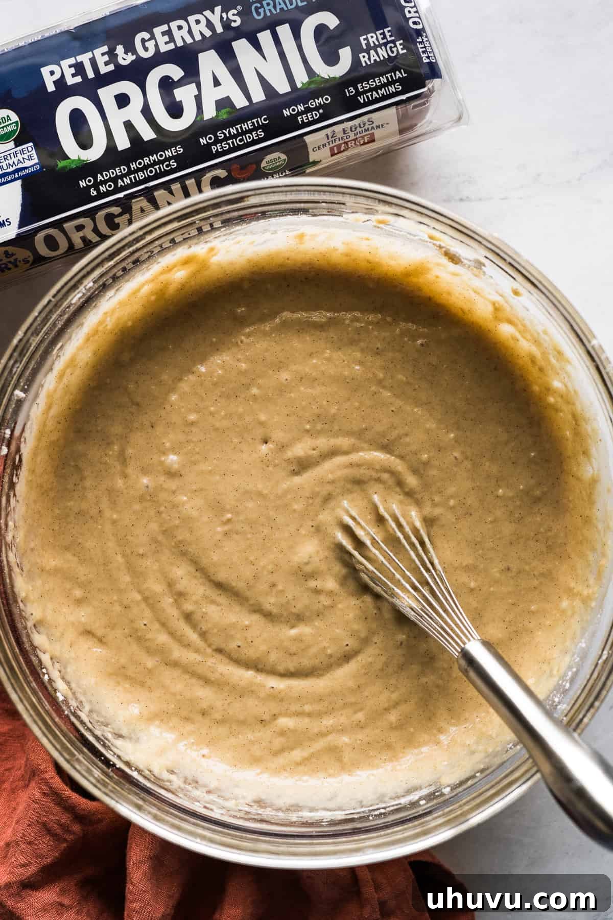 Spiced Apple Tres Leches Dream 4 Smooth cake batter being whisked in a glass bowl on a wooden table, showcasing the preparation of the apple tres leches cake from scratch.
