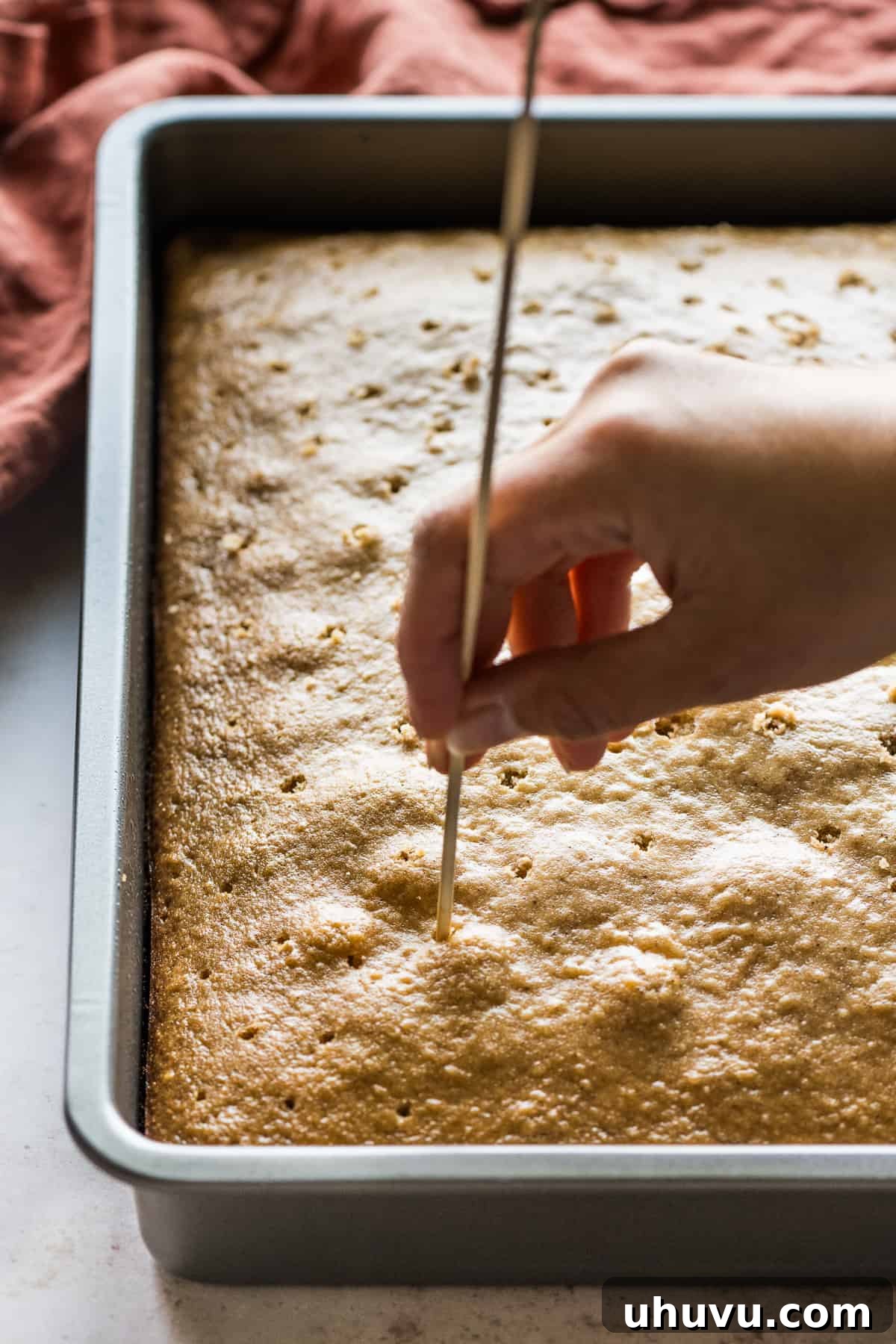 Spiced Apple Tres Leches Dream 5 A skewer creating small holes across the surface of a freshly baked apple tres leches cake, preparing it to absorb the three-milk mixture for maximum moisture.