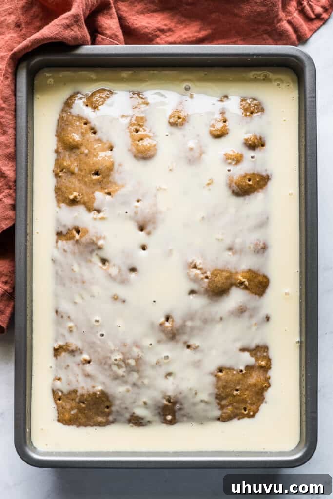 Spiced Apple Tres Leches Dream 6 The luxurious three-milk mixture being slowly poured over an apple tres leches cake, seeping into the poked holes to create a decadent, moist texture.